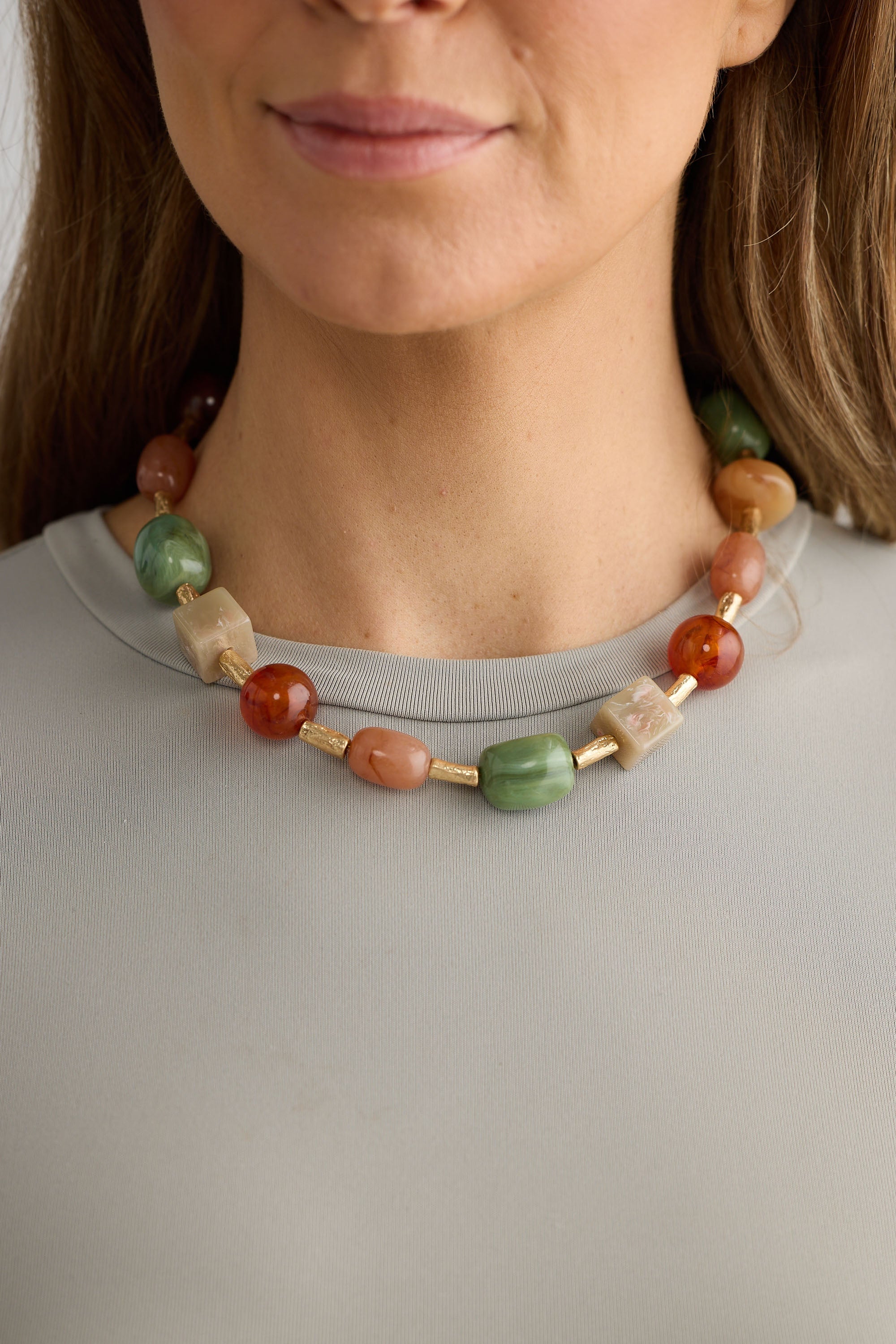 Necklace with multicolored beads worn by a person against a neutral background
