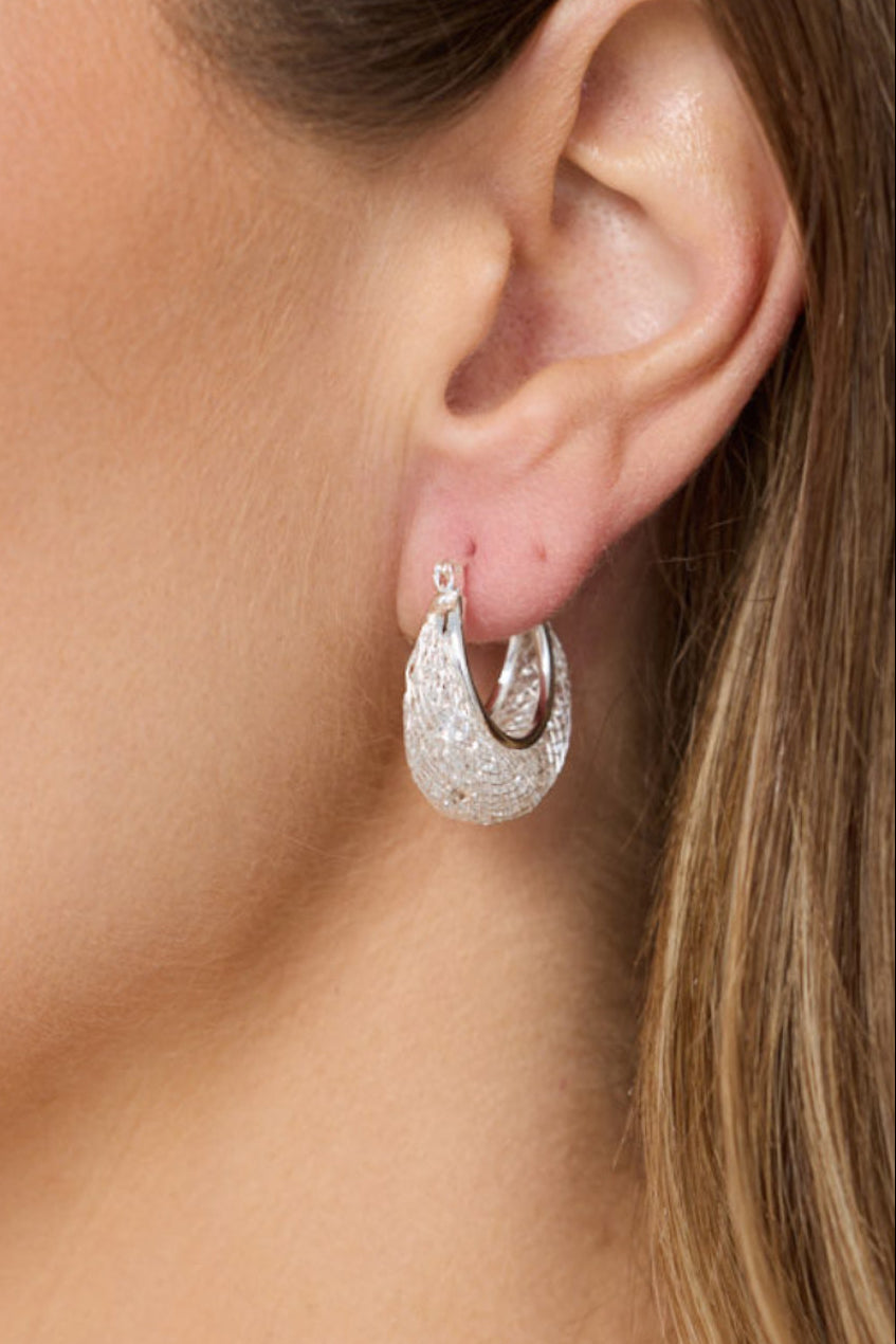 Close-up of a woman wearing silver hoop earrings with a neutral background