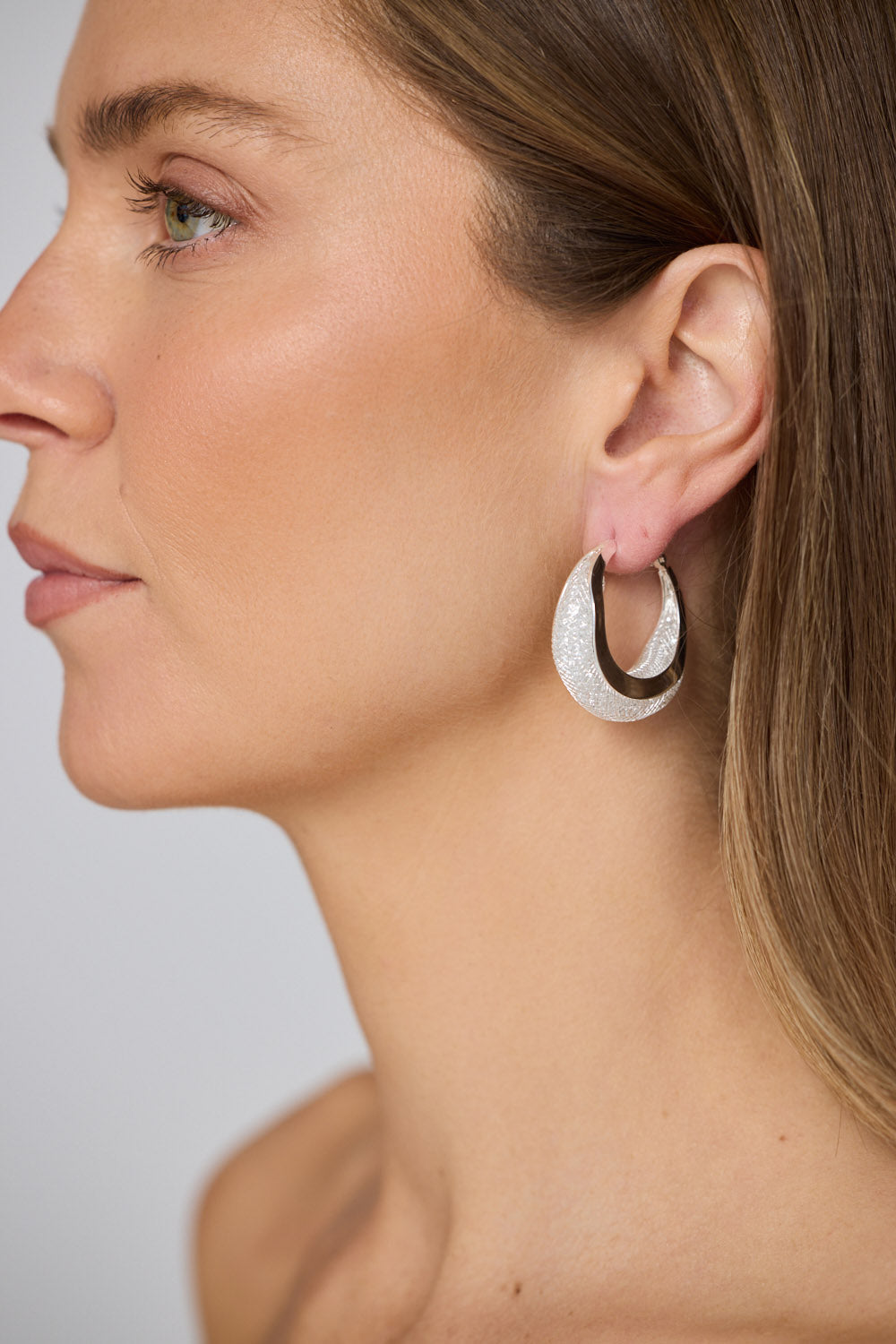Model wearing Eclipse Earrings in silver with soft textured finish, side profile view.