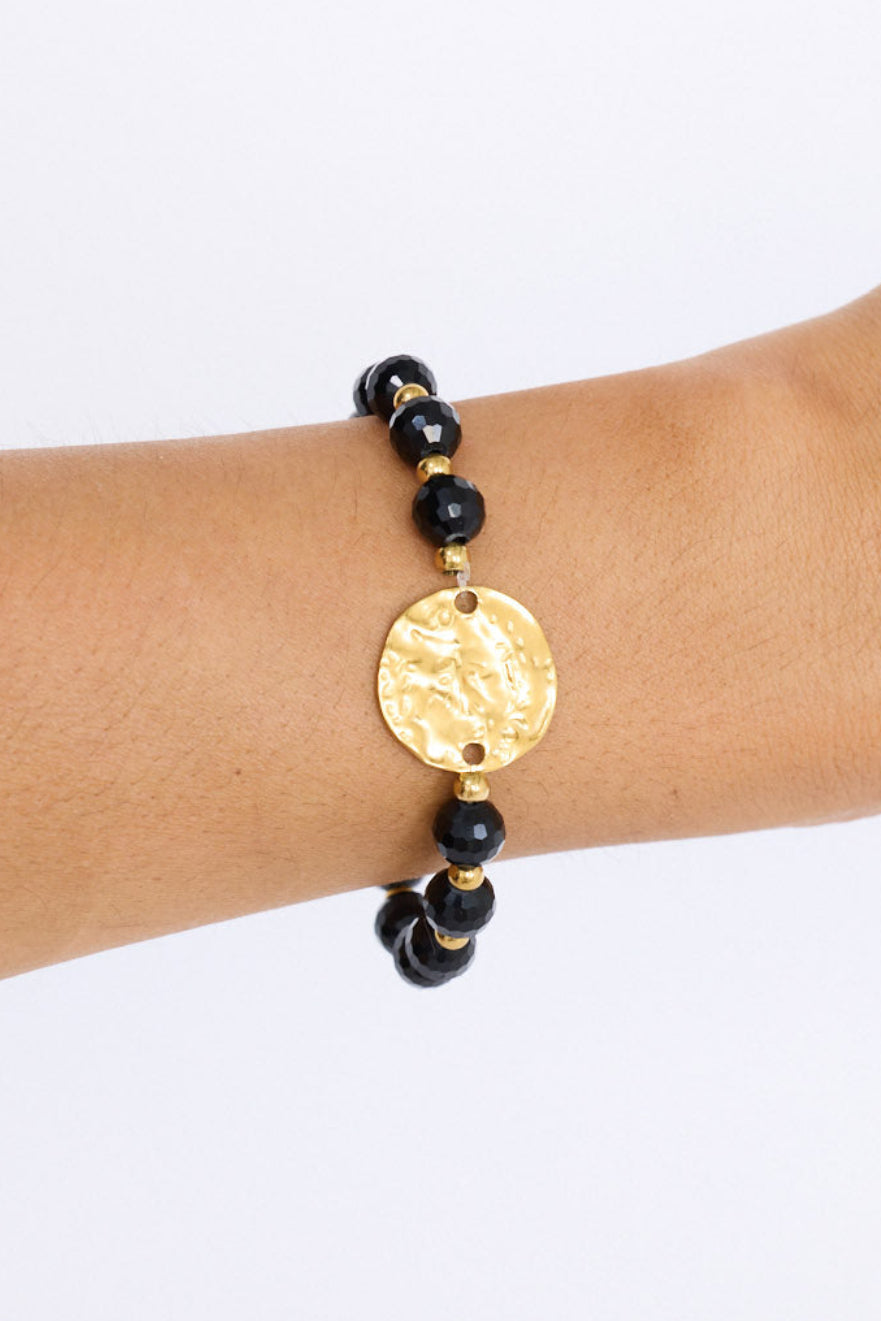 Model wearing Taylor Bracelet in black with statement gold charm detail, angled on-wrist view.