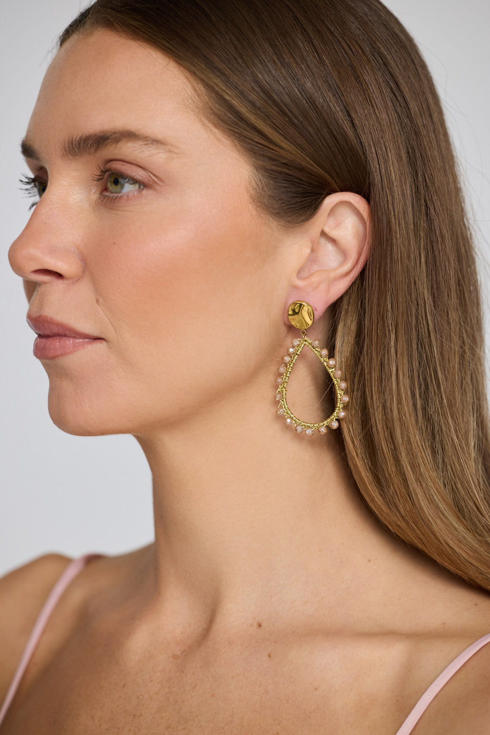 Model wearing Sawyer Earrings in blush with delicate beaded trim detailing, close-up view.