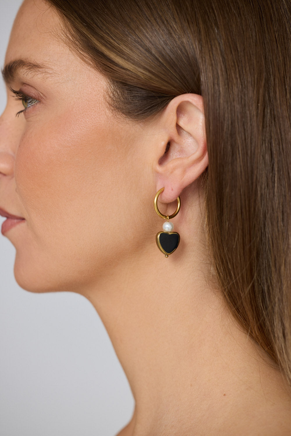Model wearing Mimi Earrings in black with bold heart charm detail, close-up view.