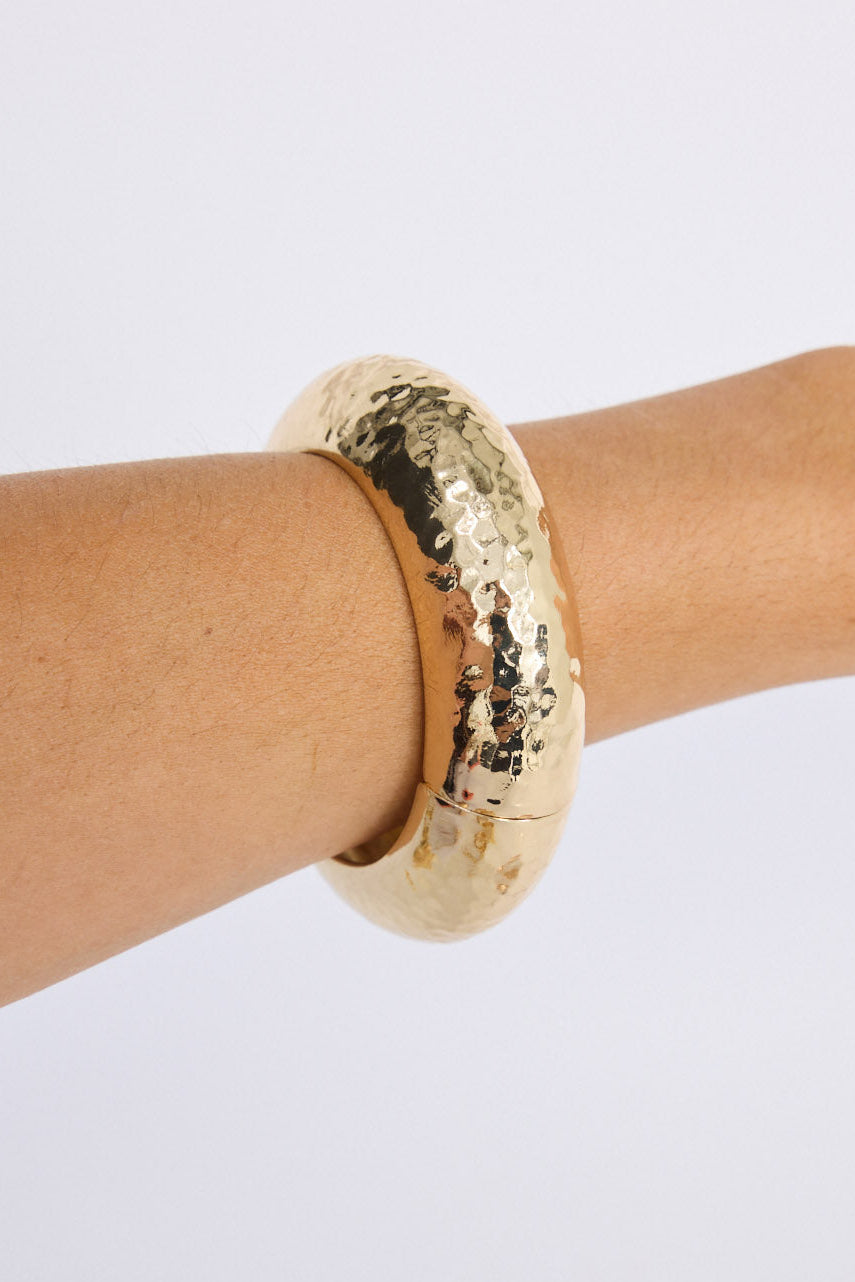 Model wearing Seville Bangle in gold with snap lock closure and hinge for easy wear, angled on-wrist view.
