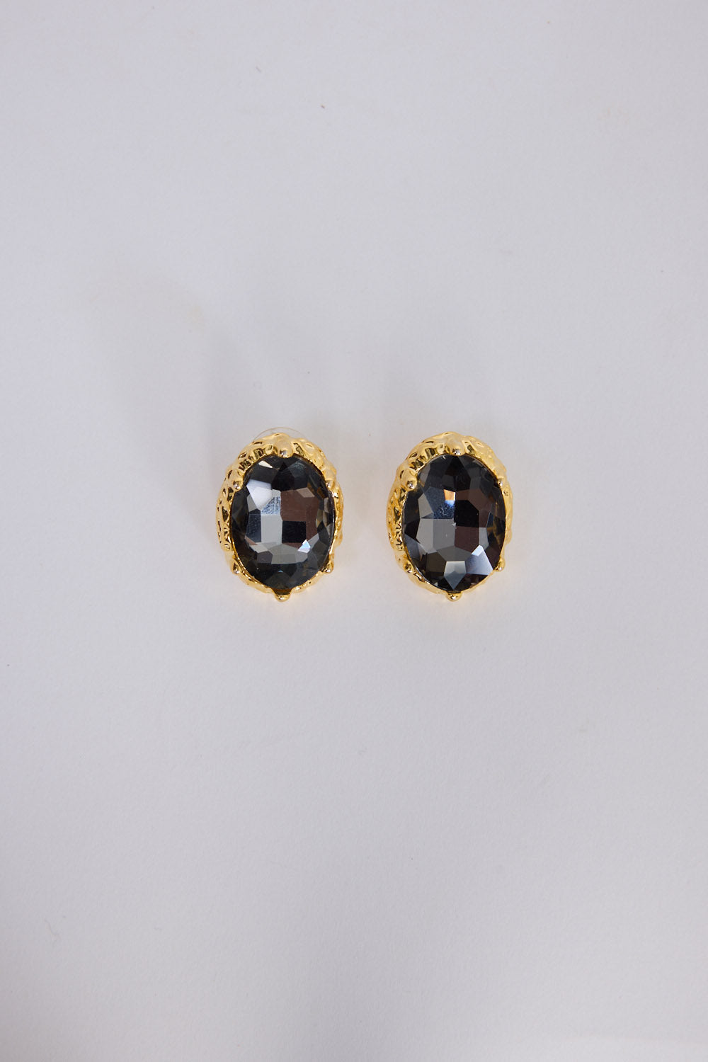 Unice Earrings in smoke with a faceted stone set in a textured gold surround, angled view.