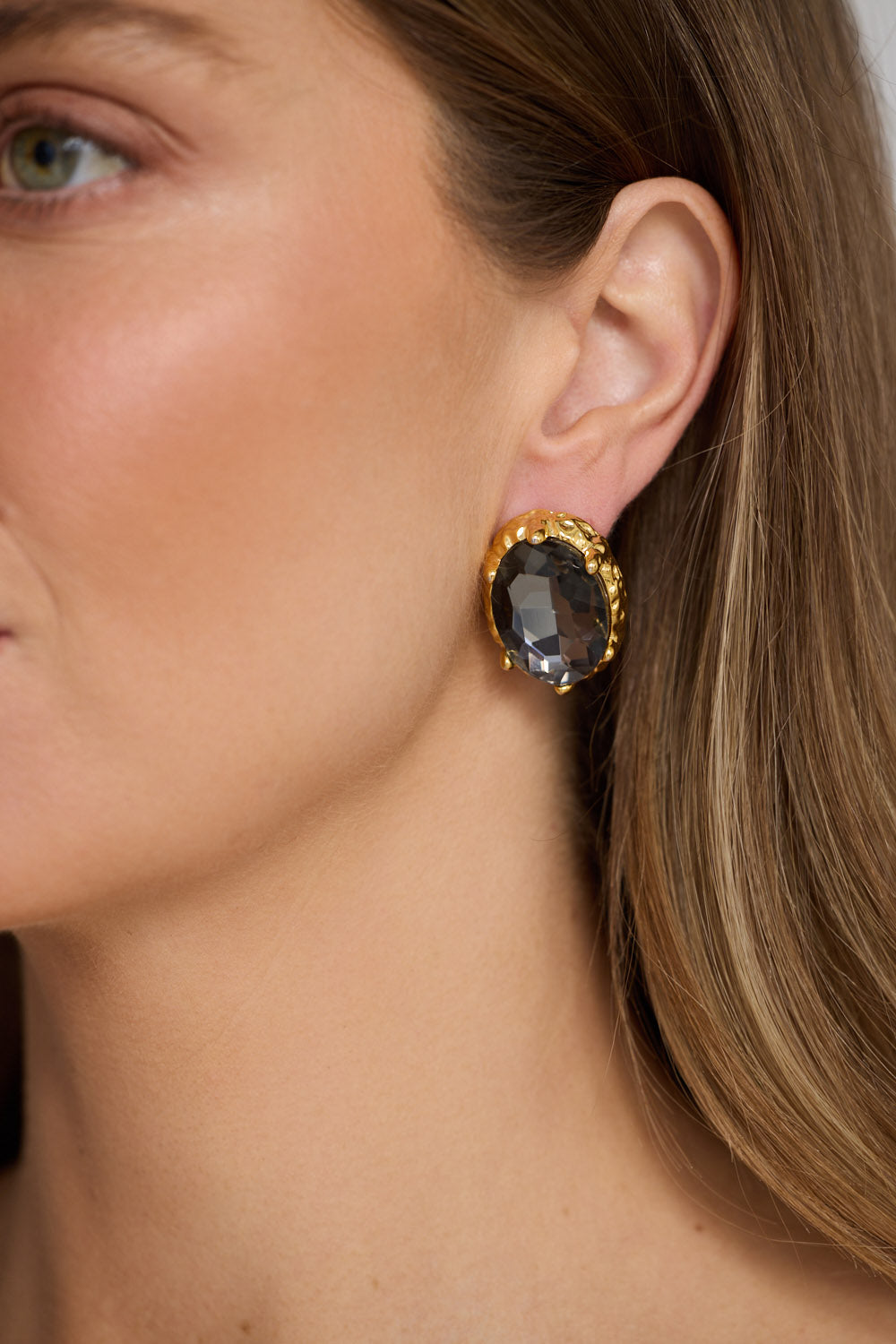 Model wearing Unice Earrings in smoke with a faceted stone set in a textured gold surround, close-up view.