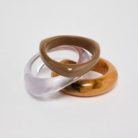 Set of three slim resin bangles in translucent lilac, warm taupe and mustard-amber marbled finishes, stacked and interlocked together on a white background