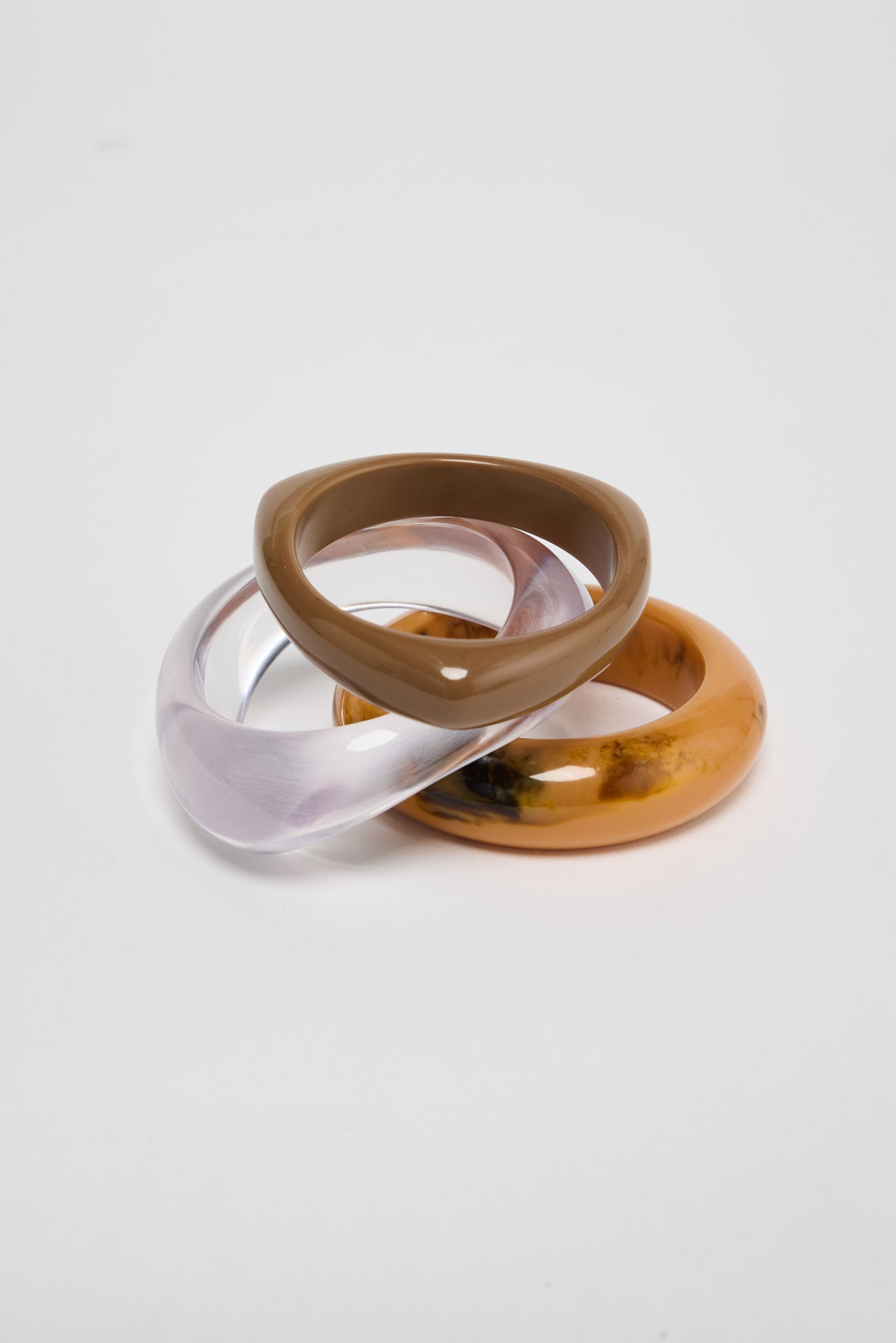 Set of three slim resin bangles in translucent lilac, warm taupe and mustard-amber marbled finishes, stacked and interlocked together on a white background