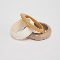 Set of three slim resin bangles in cream, honey-tan and warm taupe neutral finishes, stacked and interlocked together on a white background