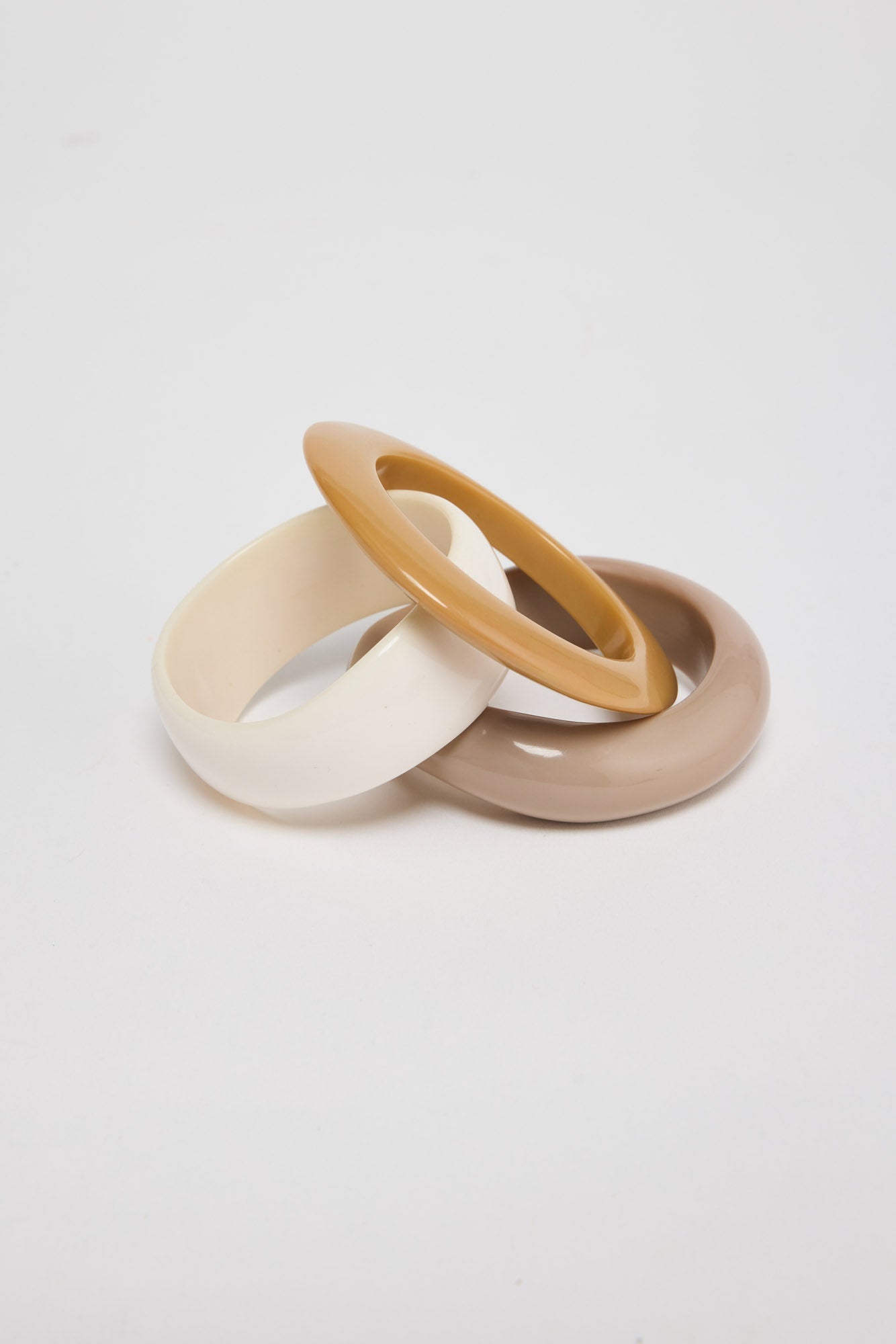 Set of three slim resin bangles in cream, honey-tan and warm taupe neutral finishes, stacked and interlocked together on a white background