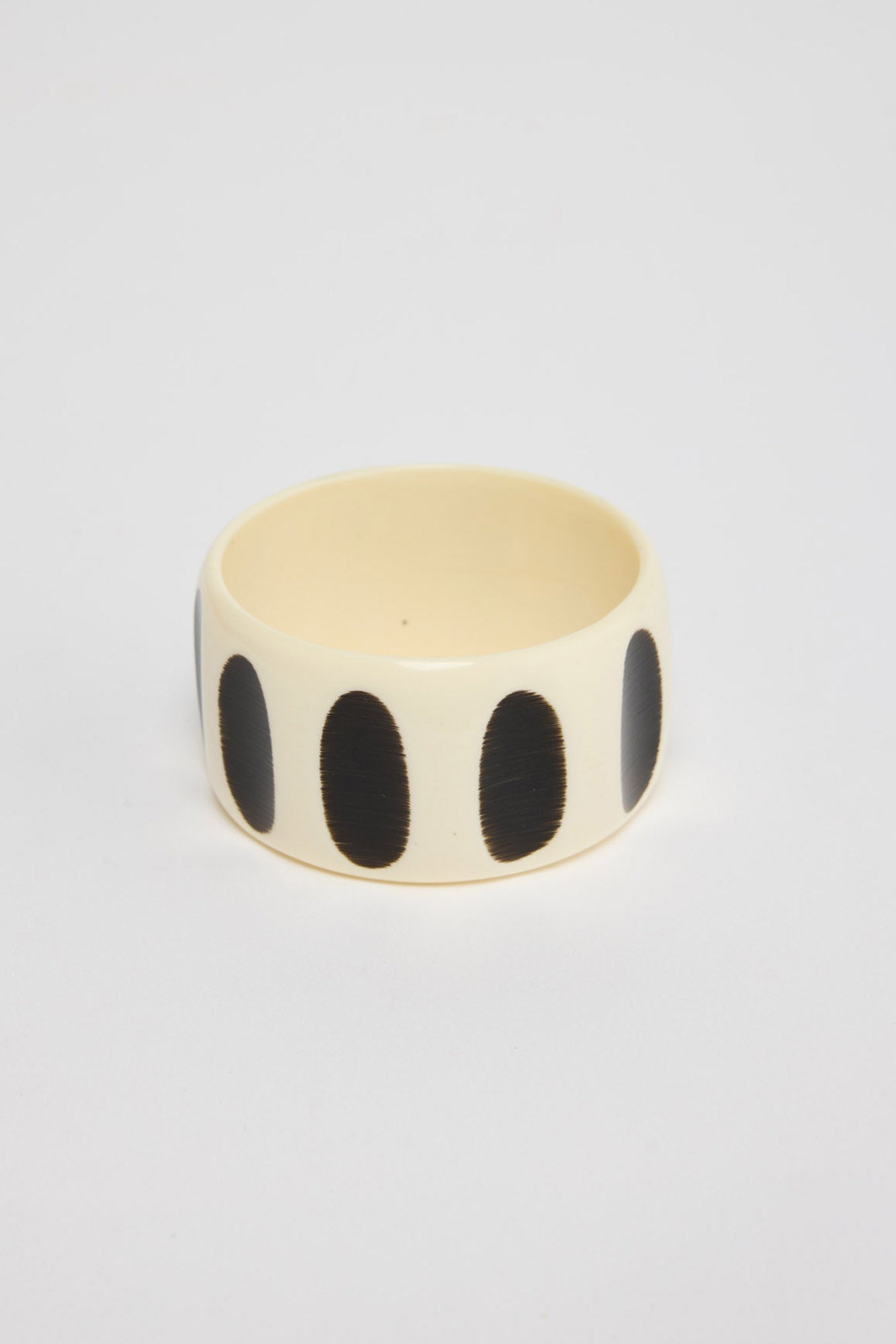 Wide chunky cream resin bangle with evenly spaced bold black oval spots around the exterior, shown at an angle on a white background