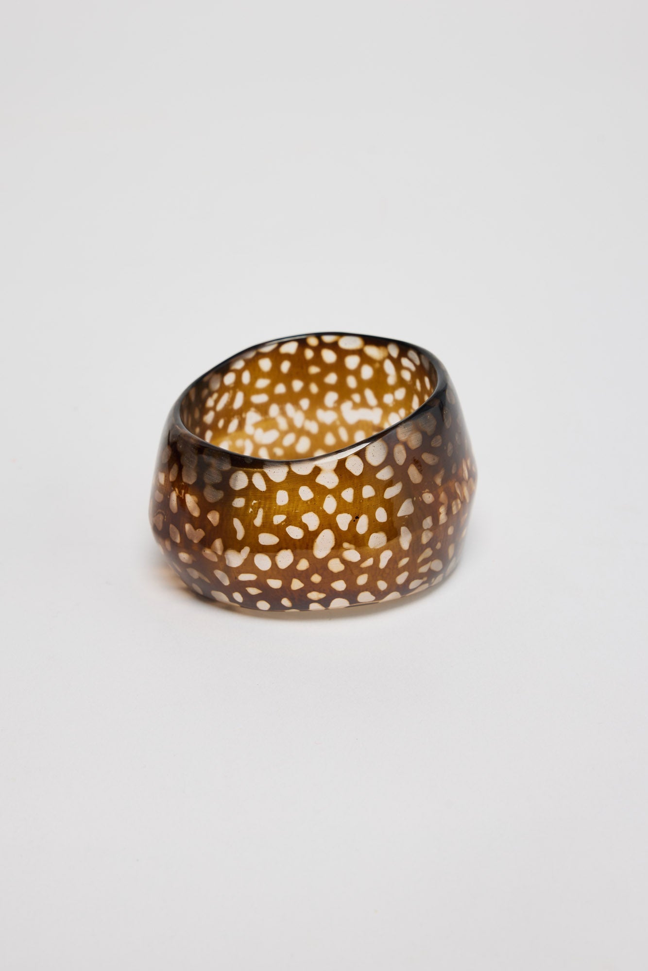Wide chunky amber-brown resin bangle with a warm tortoiseshell mottled finish, shown at an angle on a white background