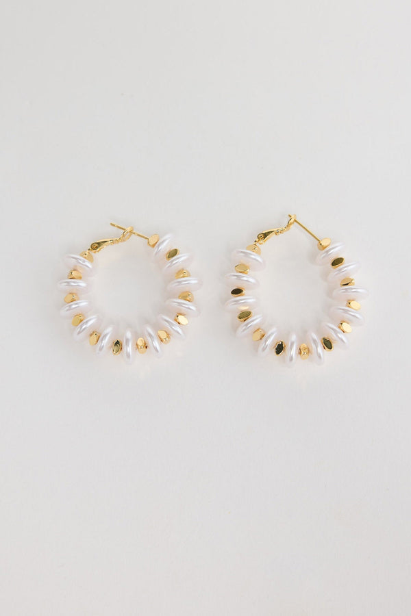 Pair of gold-tone hoop earrings made of stacked white pearl-look rondelle beads with small gold accents, laid flat on a white background