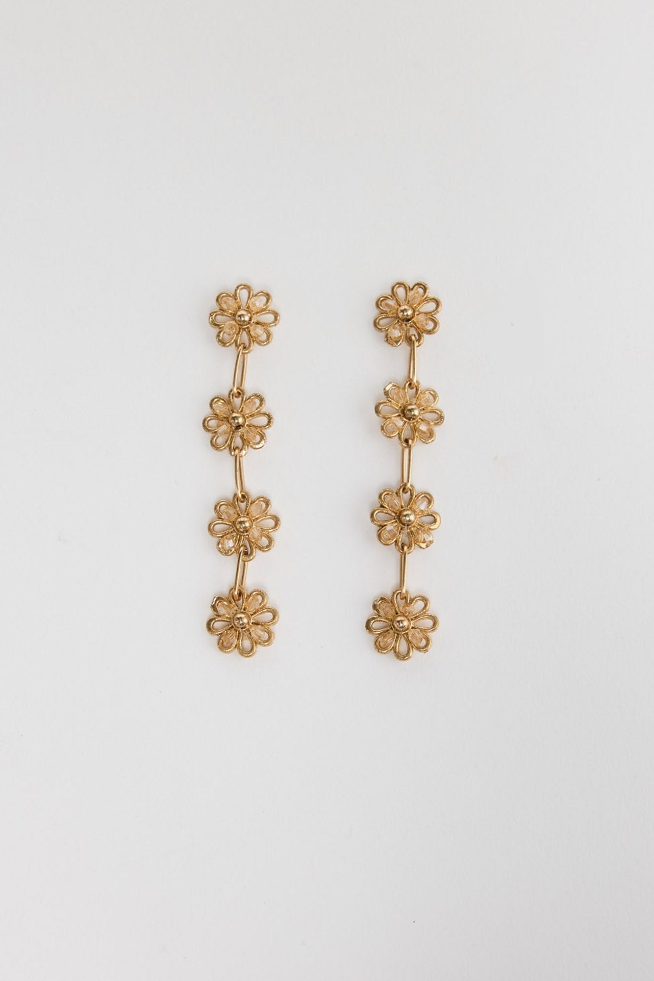 Pair of gold-tone Althea drop earrings laid flat, showing four cascading crystal-centre daisy links each