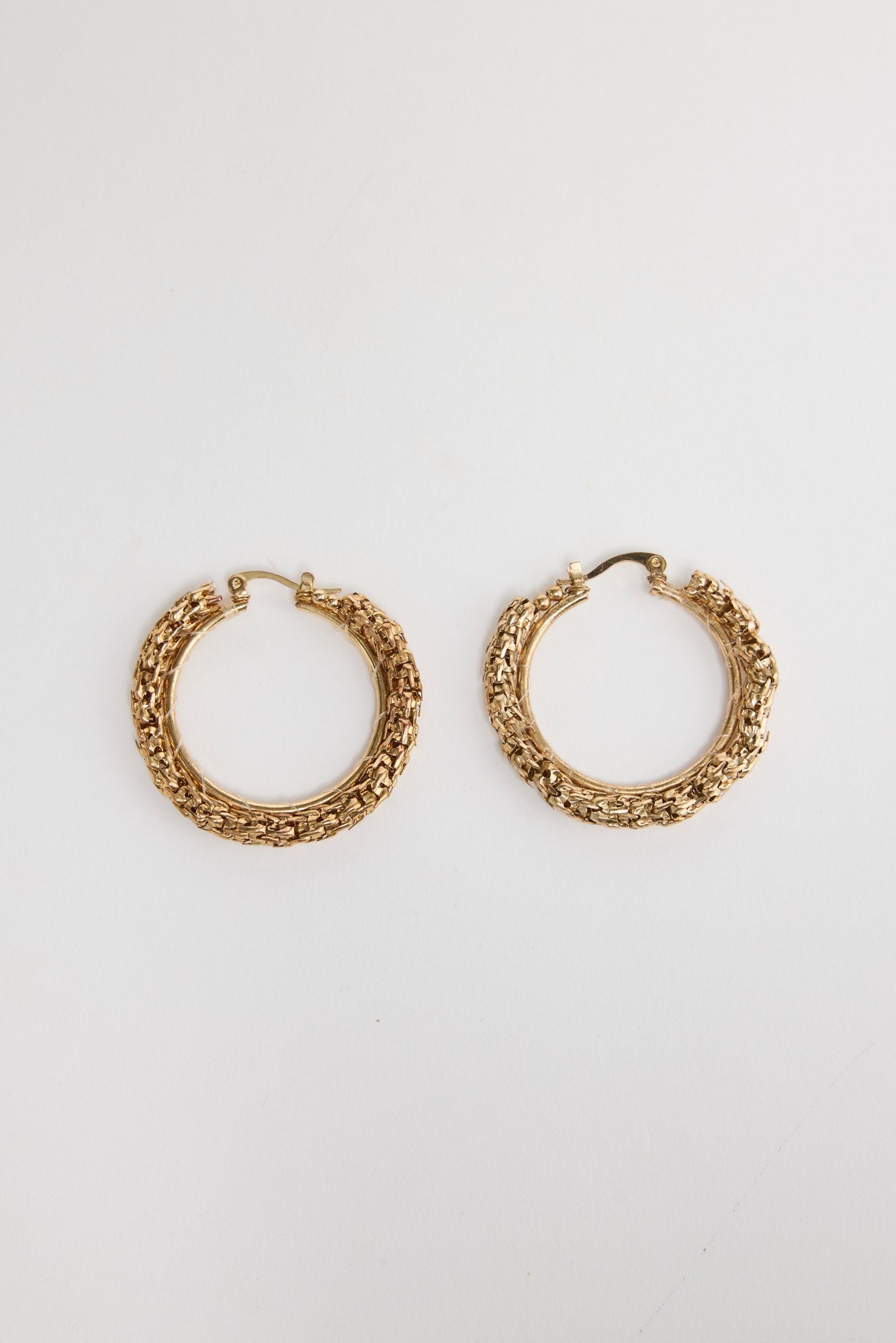 Pair of textured gold-tone Poppy hoop earrings laid flat, showing the woven metallic surface detail
