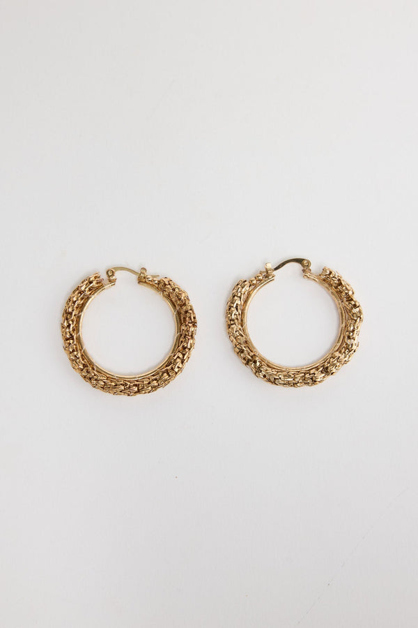 Pair of textured gold-tone Poppy hoop earrings laid flat, showing the woven metallic surface detail