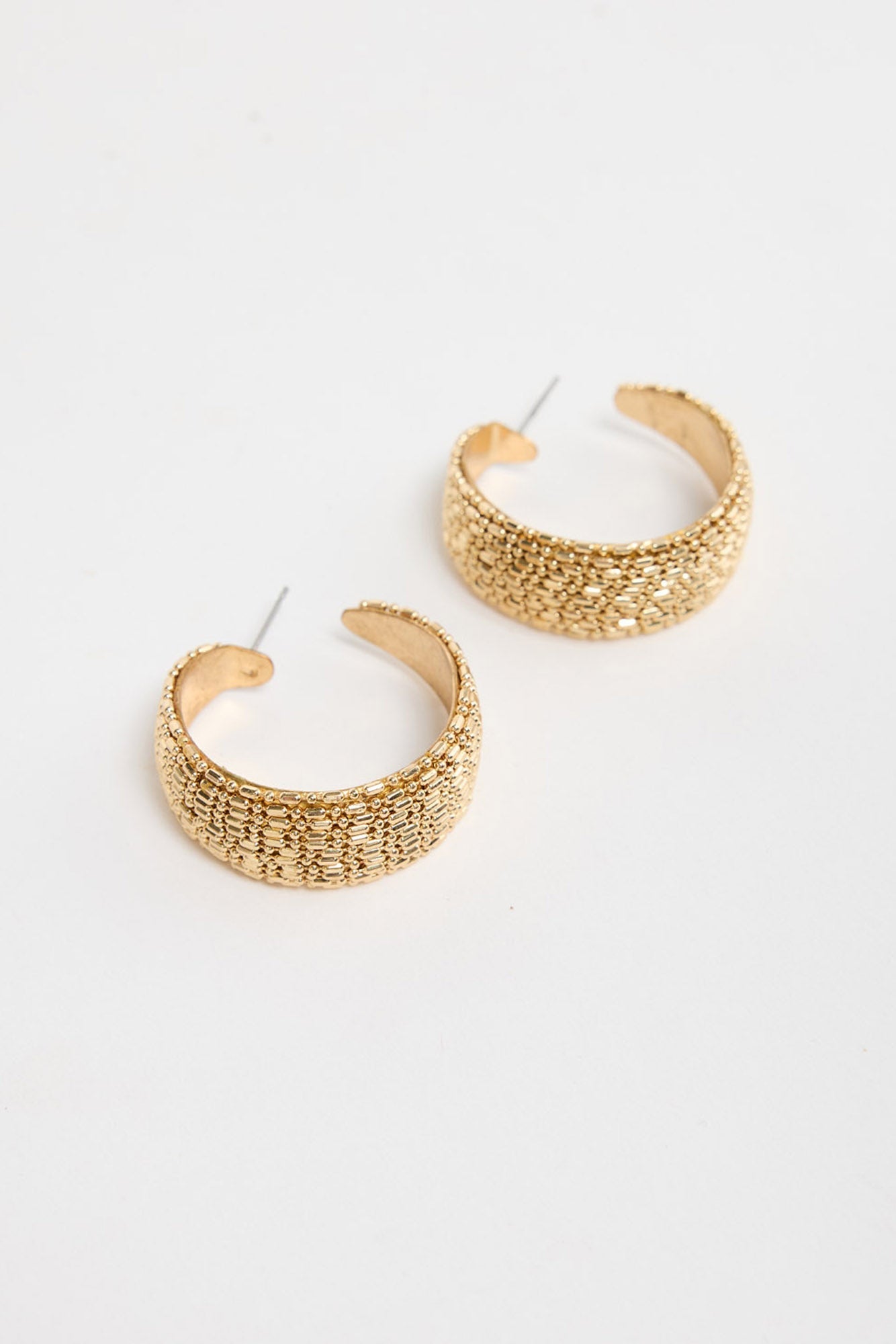 Pair of wide textured gold-tone Ione huggie earrings laid flat, showing the raised woven pattern