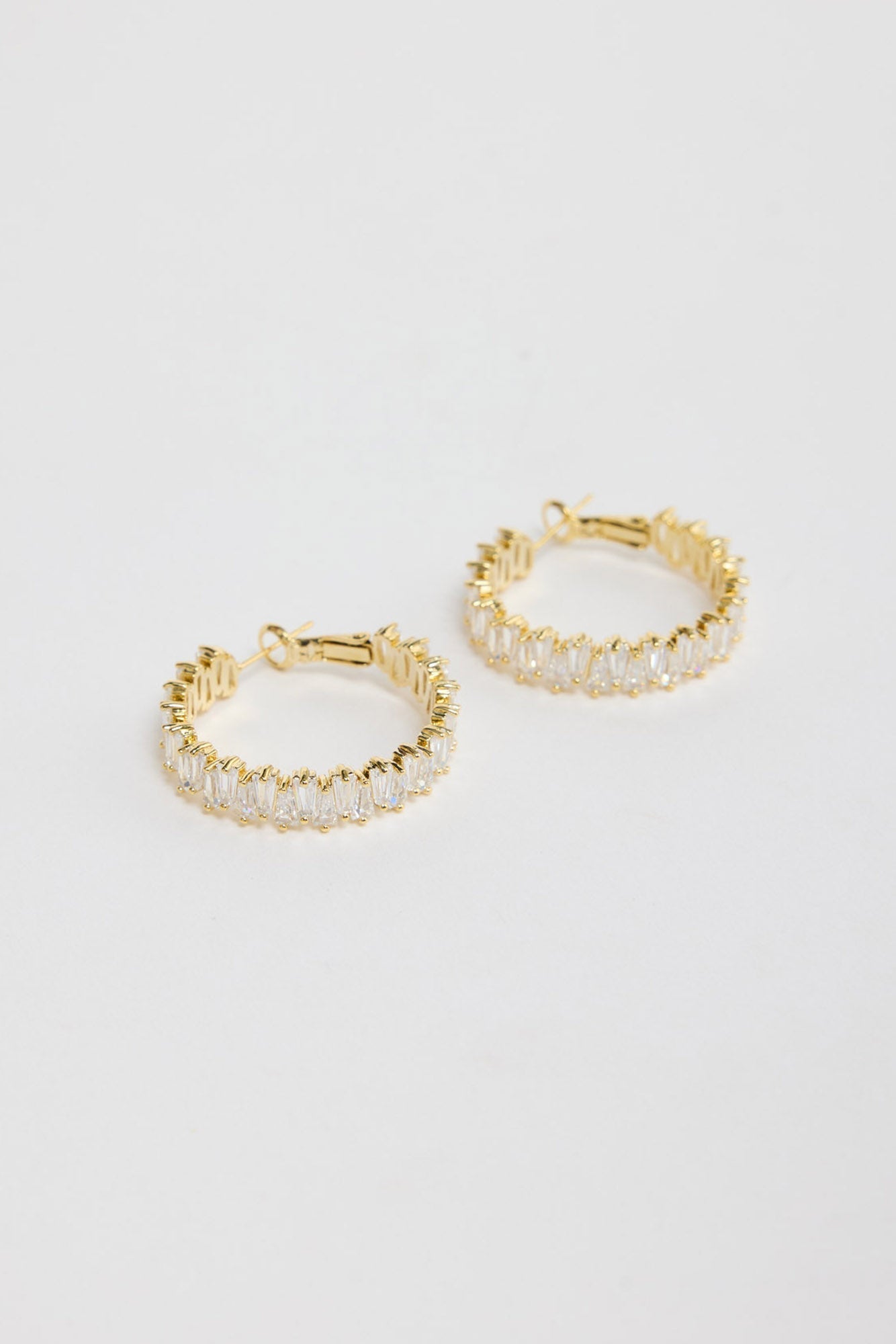 Oasis Earrings in Gold – gold-tone hoop earrings fully set with sparkling baguette crystals, shown flat on a white background.