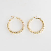 Neela Earrings in Gold – twisted, textured gold-tone hoop earrings shown flat on a white background.