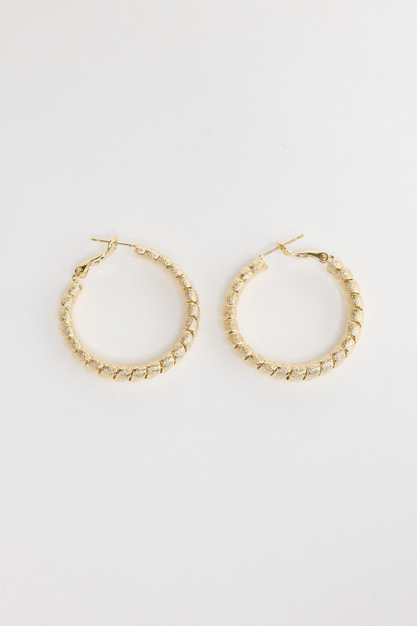 Neela Earrings in Gold – twisted, textured gold-tone hoop earrings shown flat on a white background.