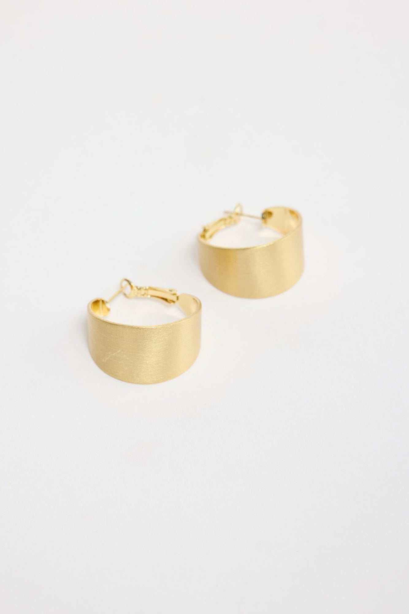 Siren Earrings in Gold – wide brushed gold-tone hoop earrings shown flat on a white background.