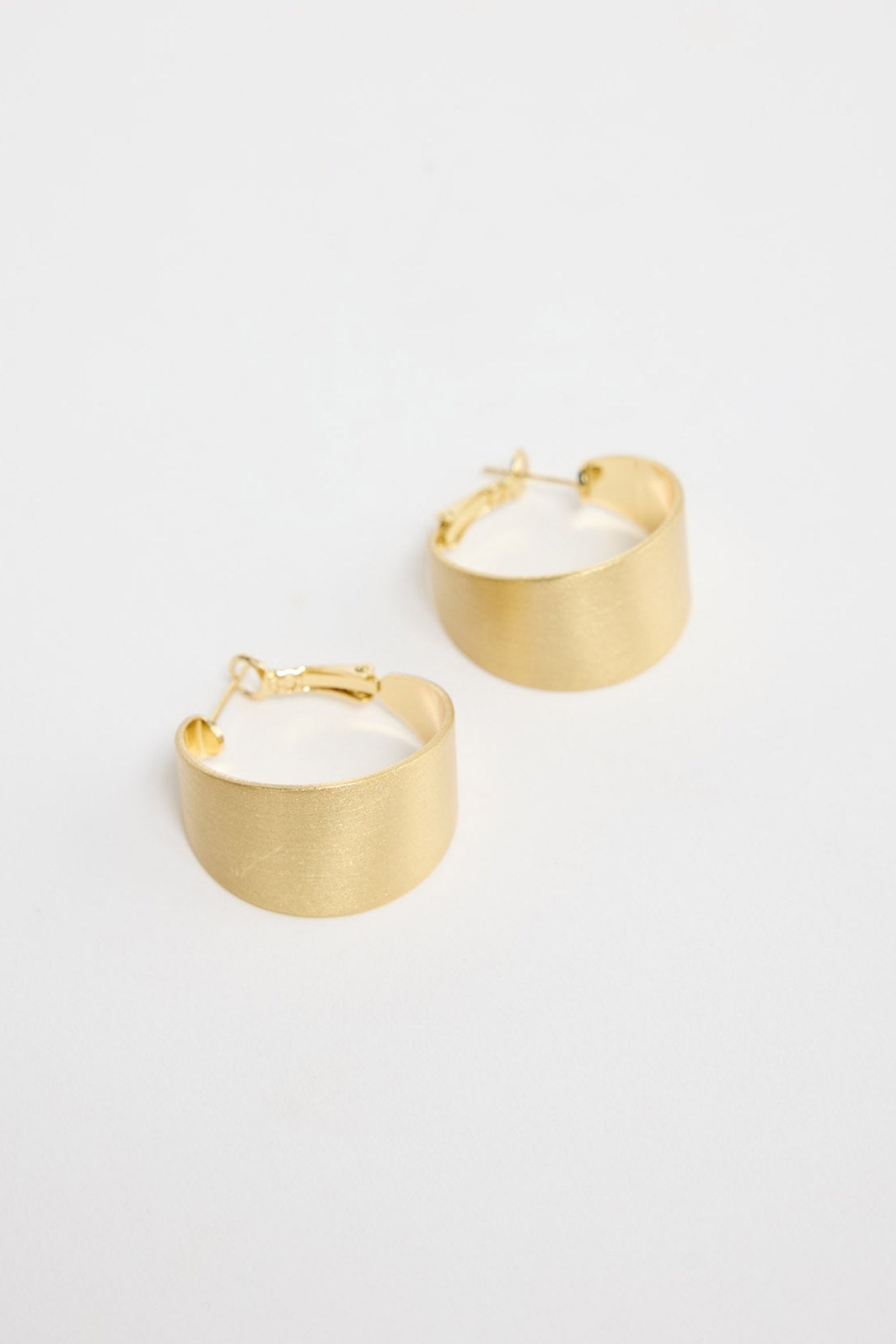 Siren Earrings in Gold worn on the ear, showing the wide hoop silhouette against the lobe.