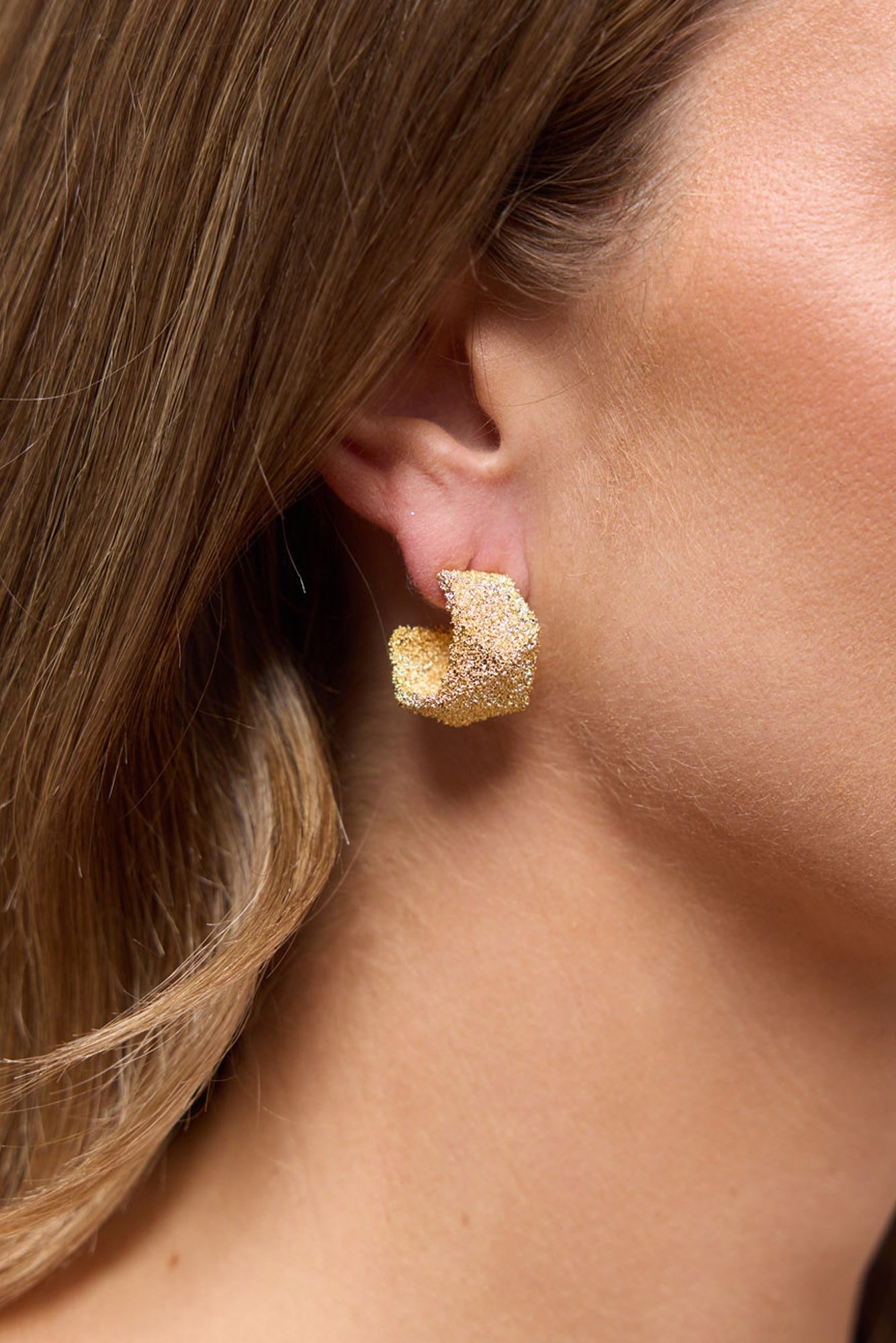 Catalina Earrings in Gold worn on the ear, showing the textured gold hoop close to the lobe.