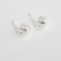 Lagoona Earrings in Silver – sculptural curved silver-tone teardrop earrings shown flat on a white background.