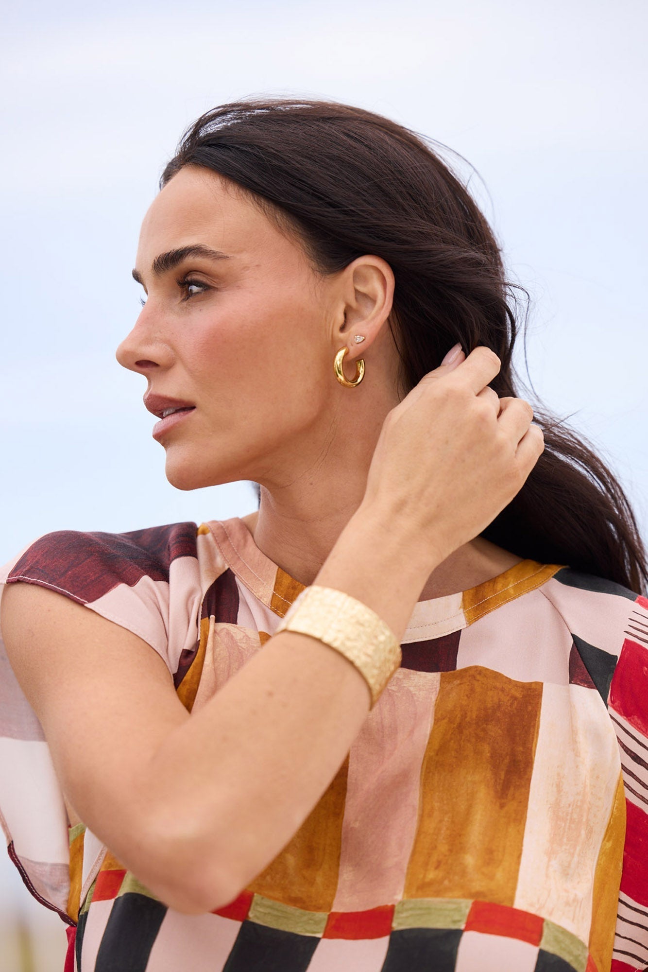 Model wearing Thick Hoops L in Gold on the ear in a profile campaign shot.