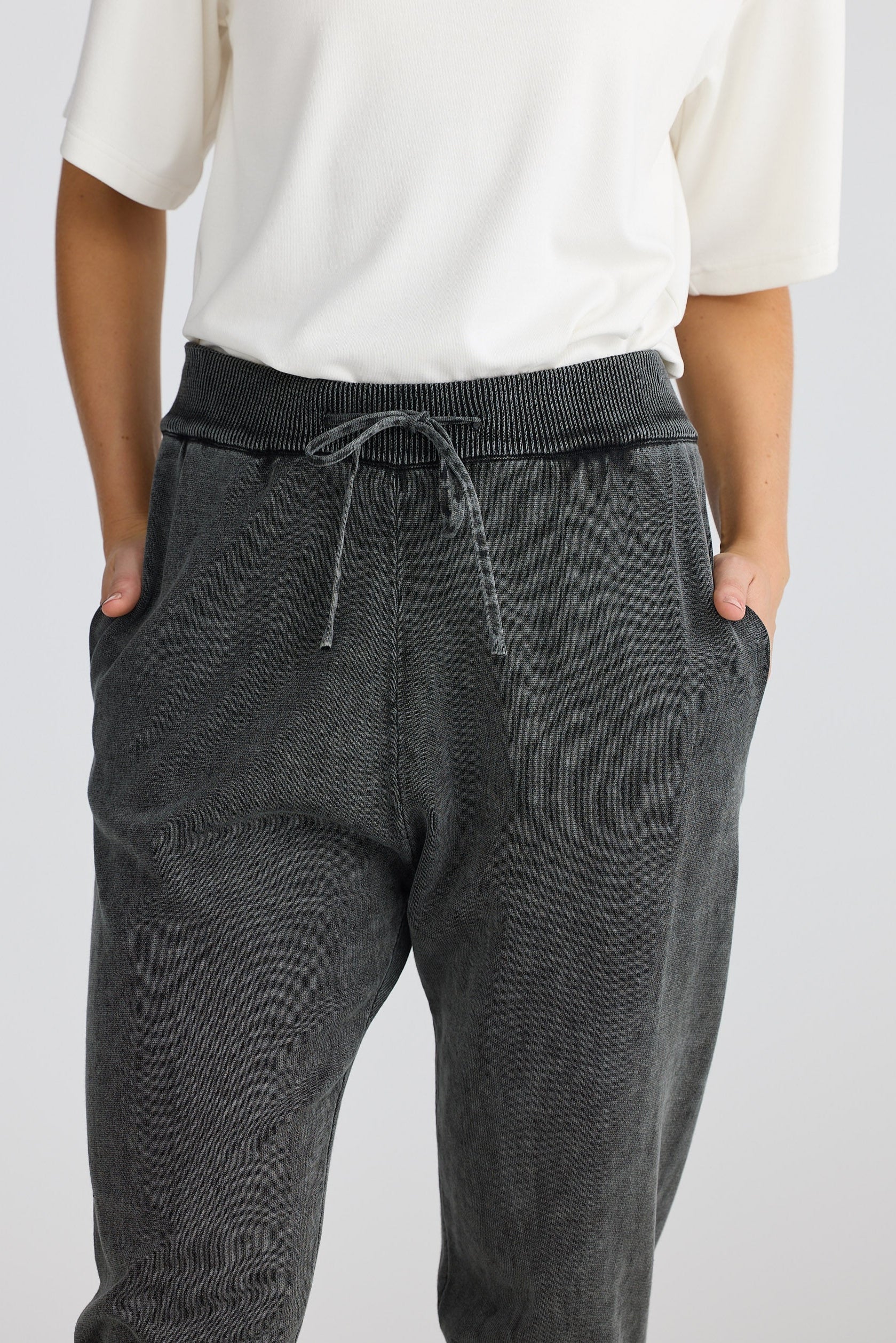 Person wearing dark gray jogger pants with a white top on a light gray background