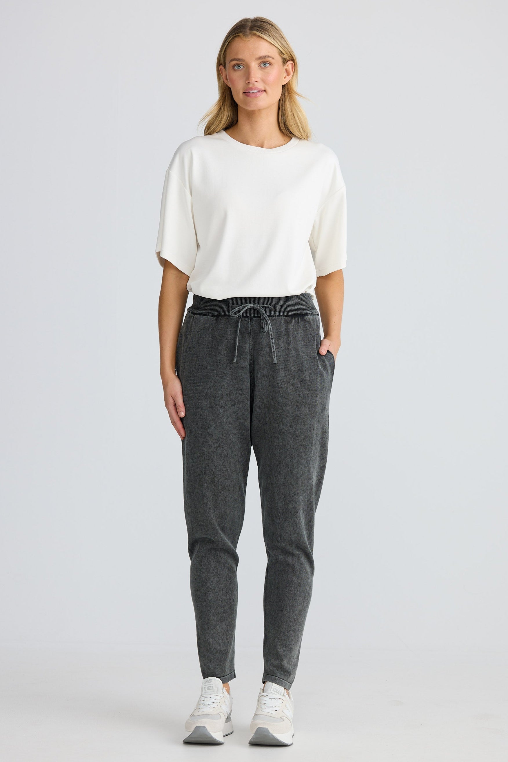 Woman wearing a white top and gray sweatpants on a light gray background