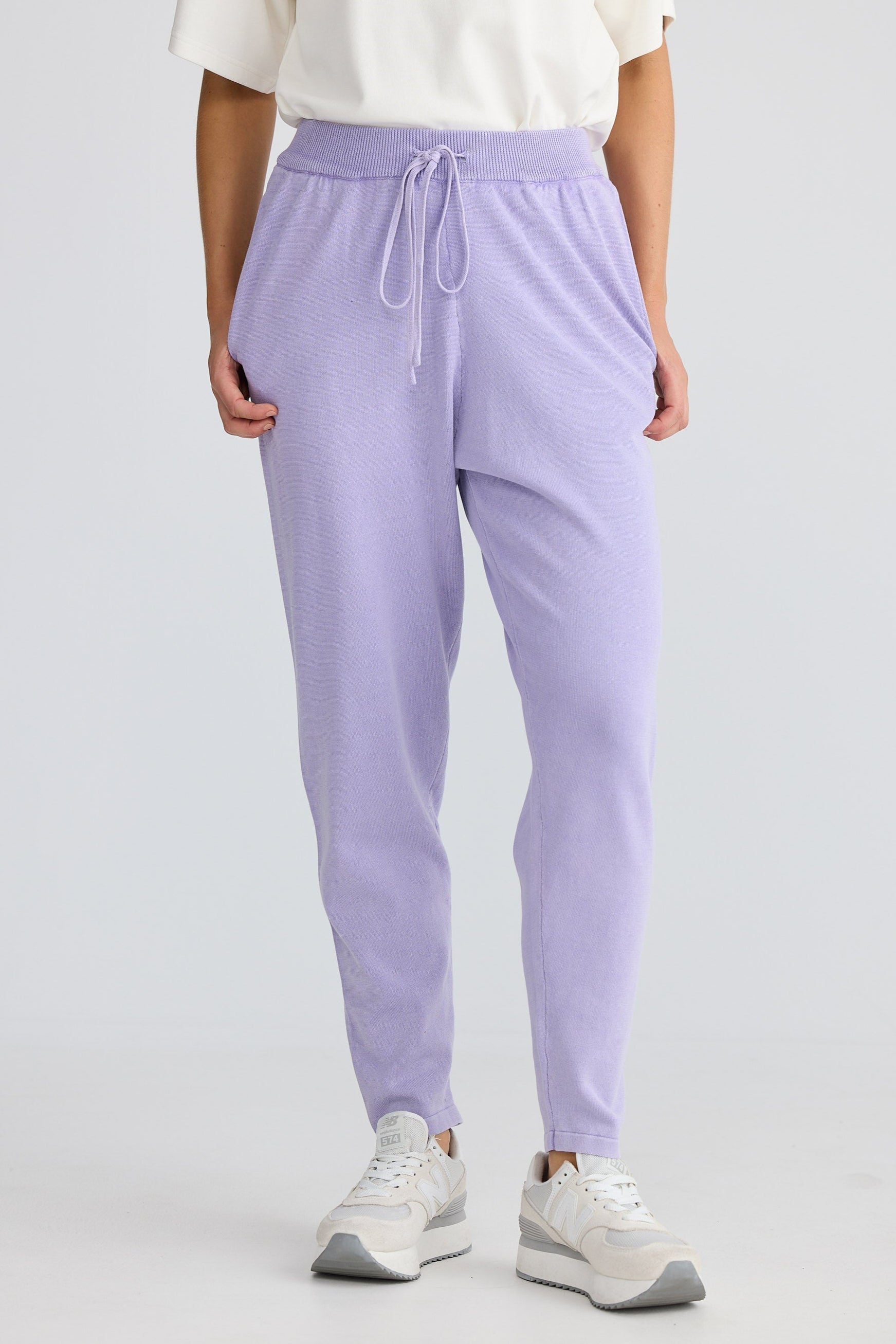 Person wearing lavender jogger pants and white sneakers on a light gray background