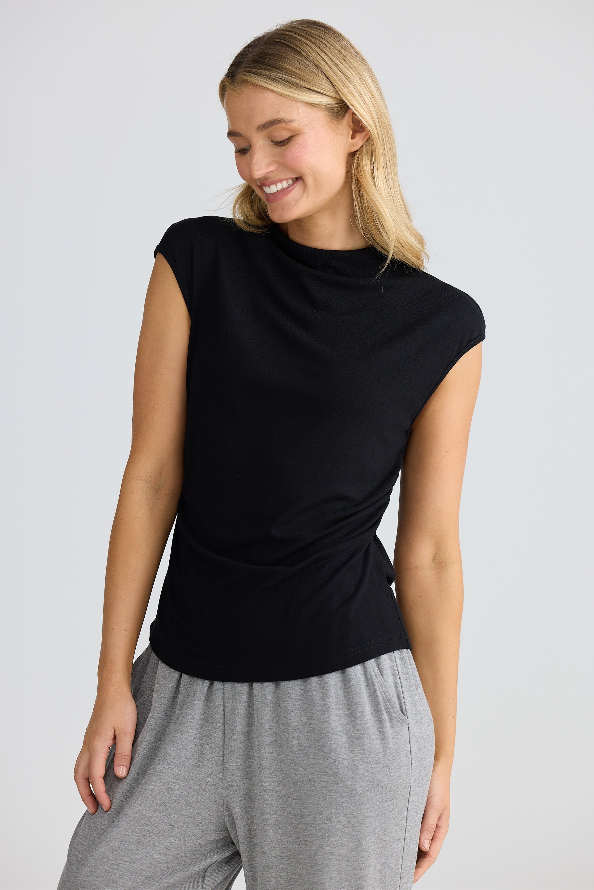 Woman wearing a black short sleeve top and gray pants on a light gray background