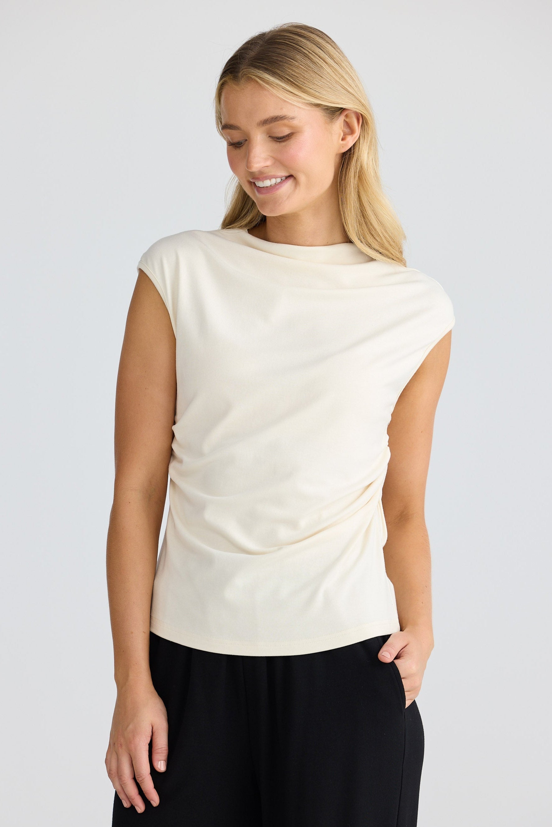 Woman wearing a cream short sleeve top and black pants on a white background