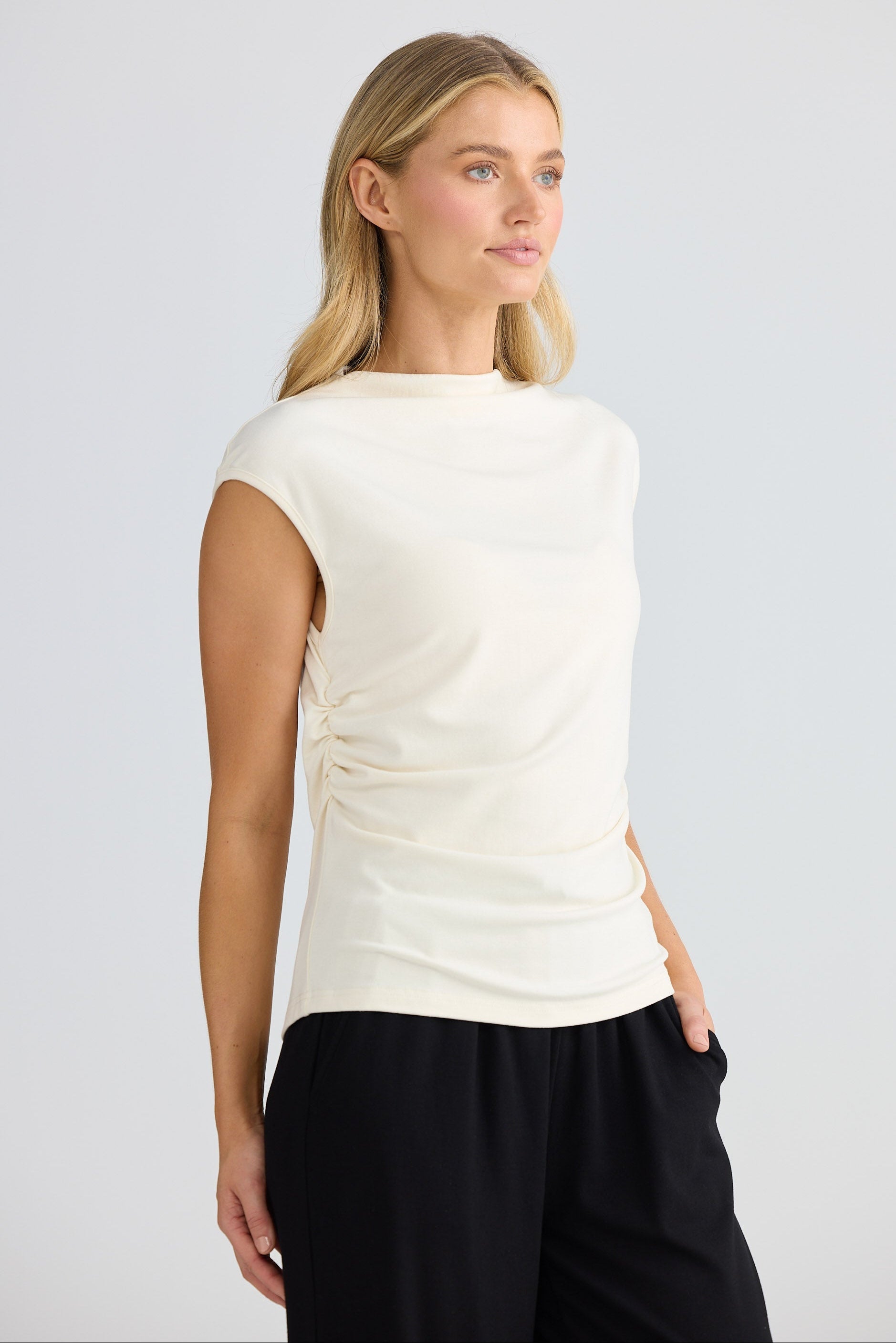 Woman wearing a cream short sleeve top and black pants on a light gray background