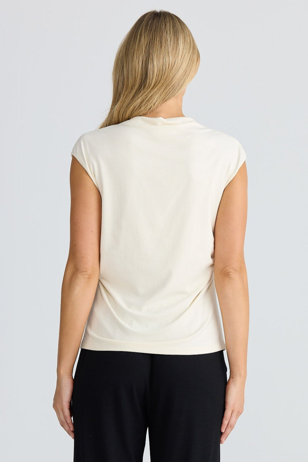 Woman wearing a cream top and black pants on a plain background