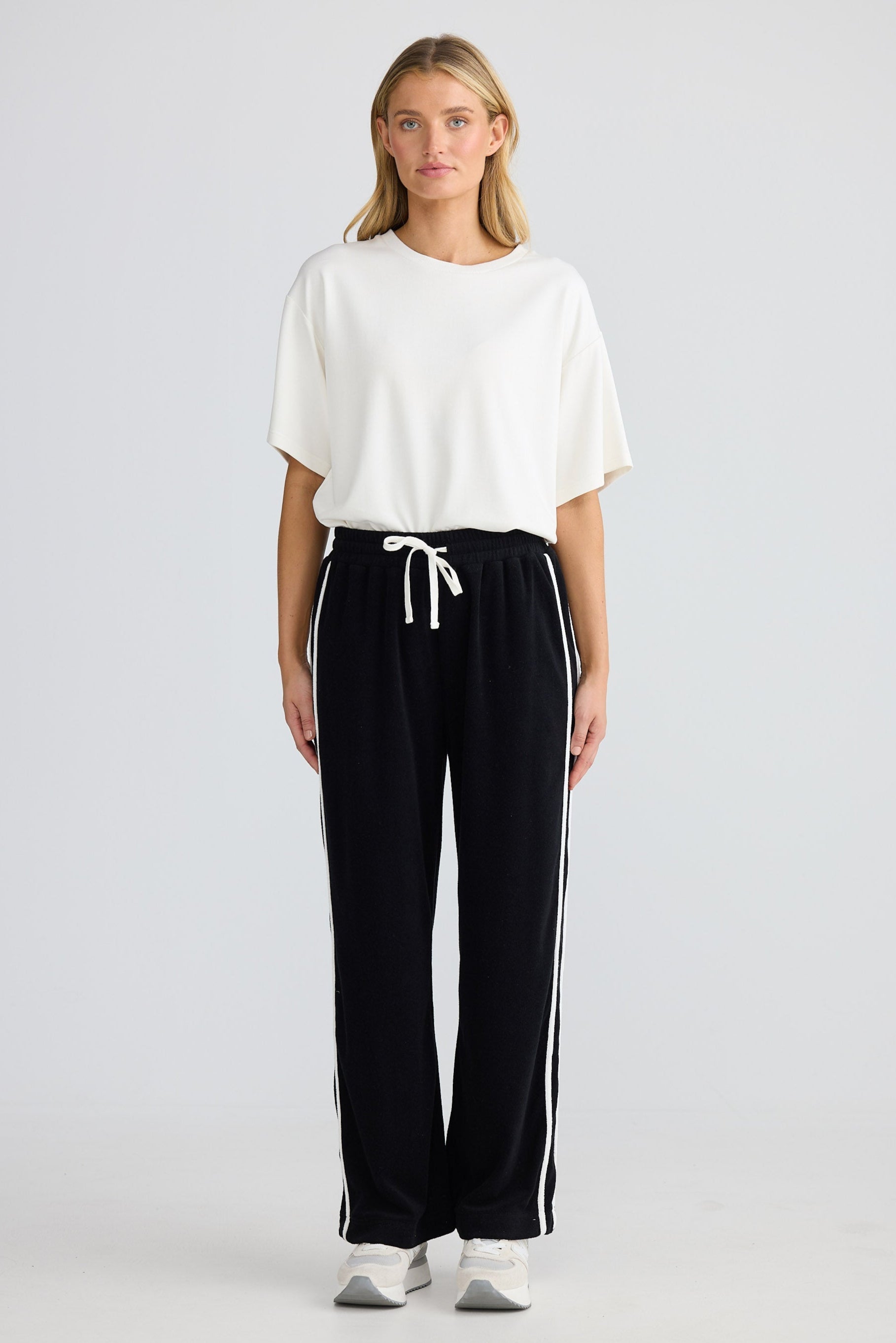 Woman wearing a white top and black pants with a stripe on a light gray background