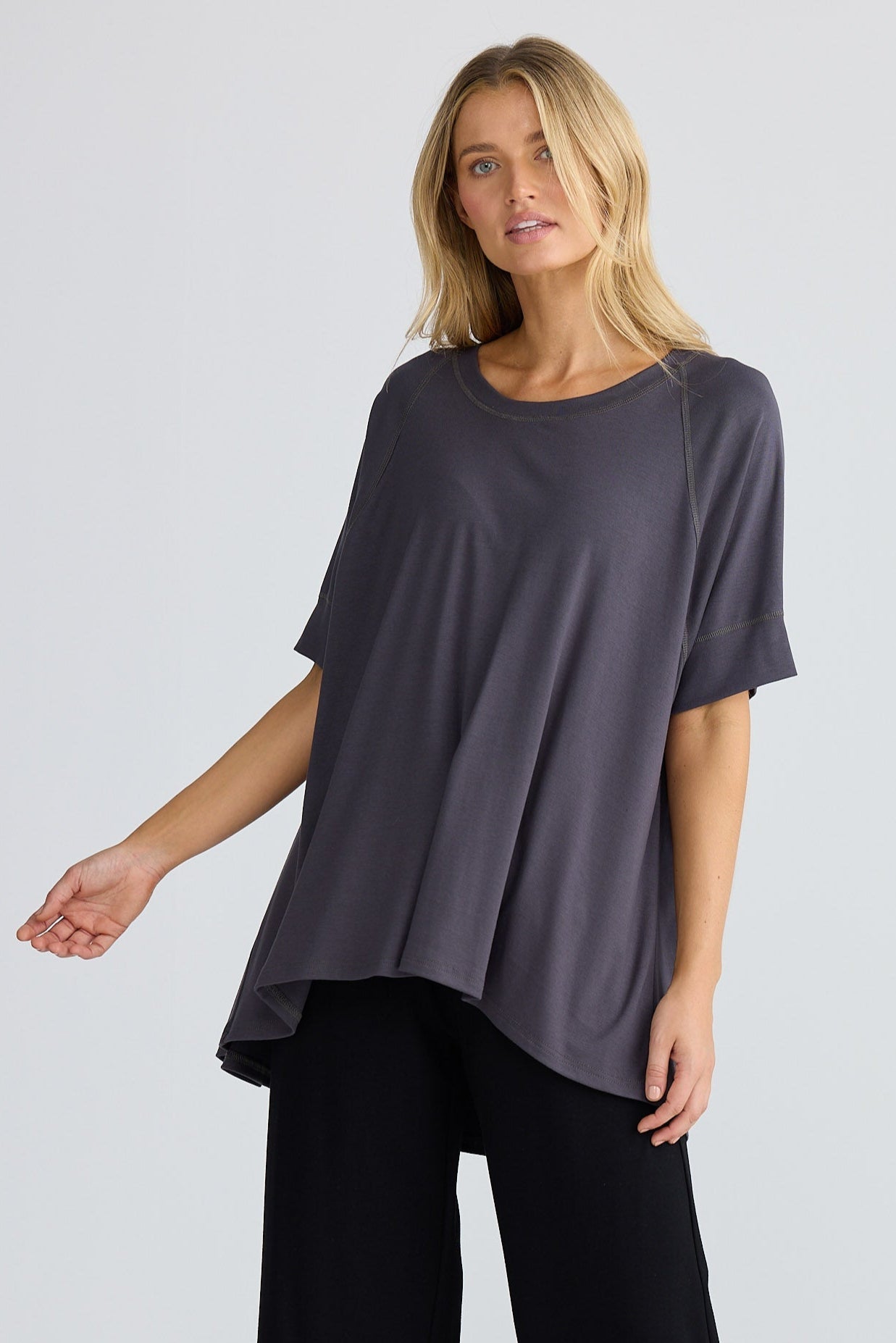 Woman wearing a dark gray oversized top and black pants on a white background