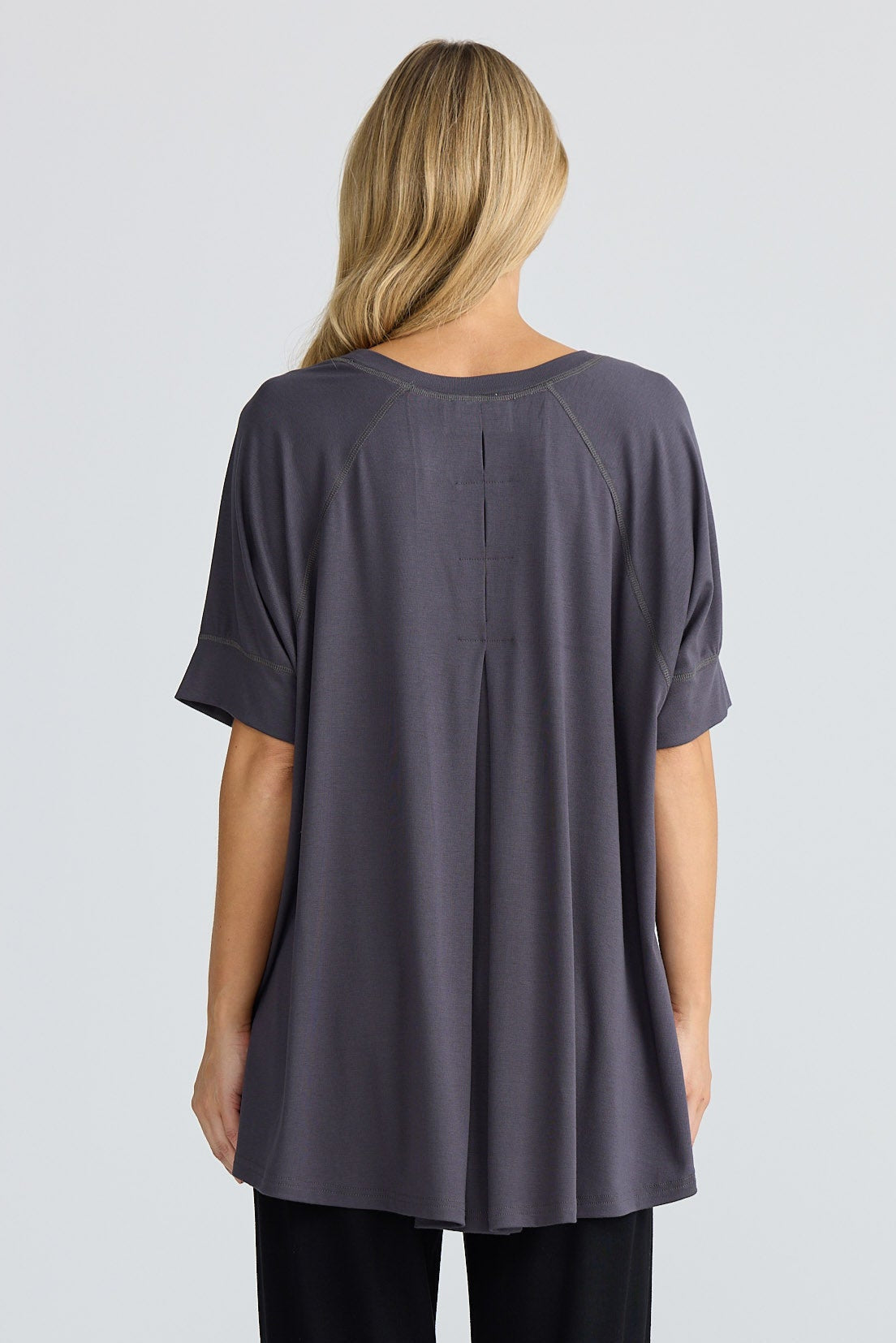 Woman wearing a grey oversized top and black pants on a white background