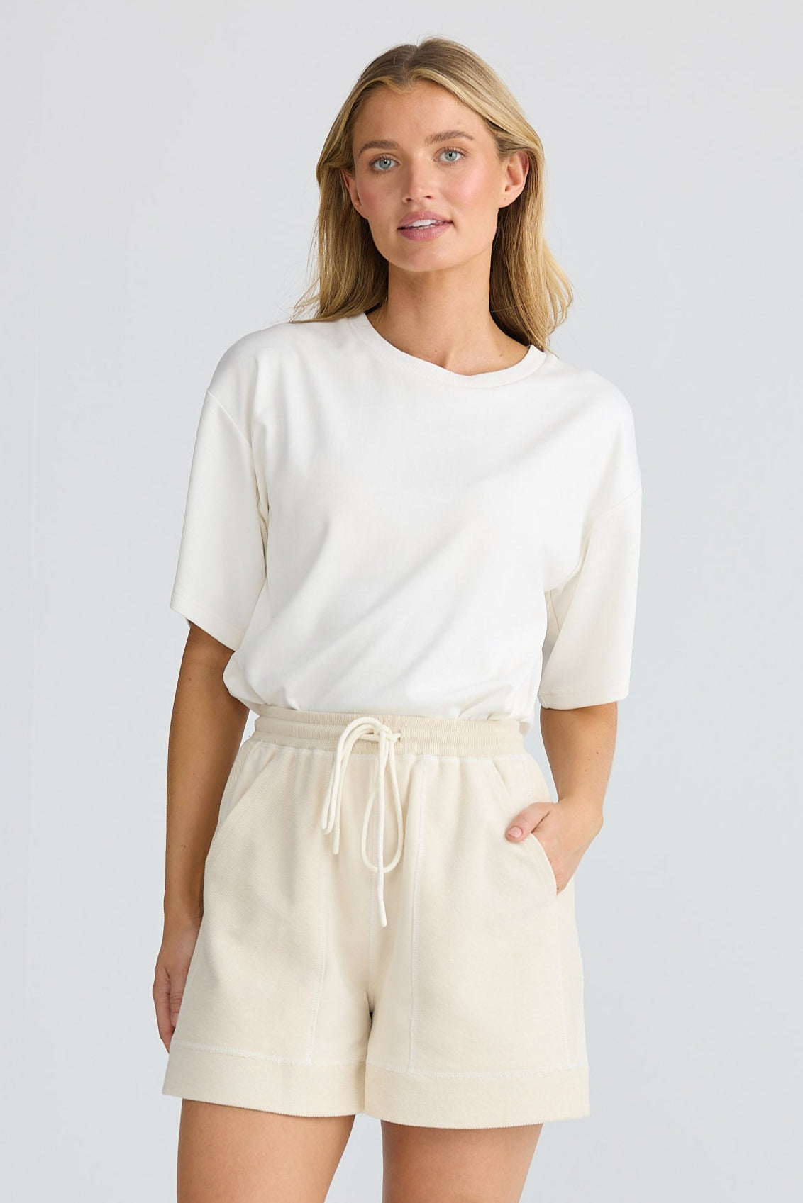 Woman wearing a white top and beige shorts on a light gray background