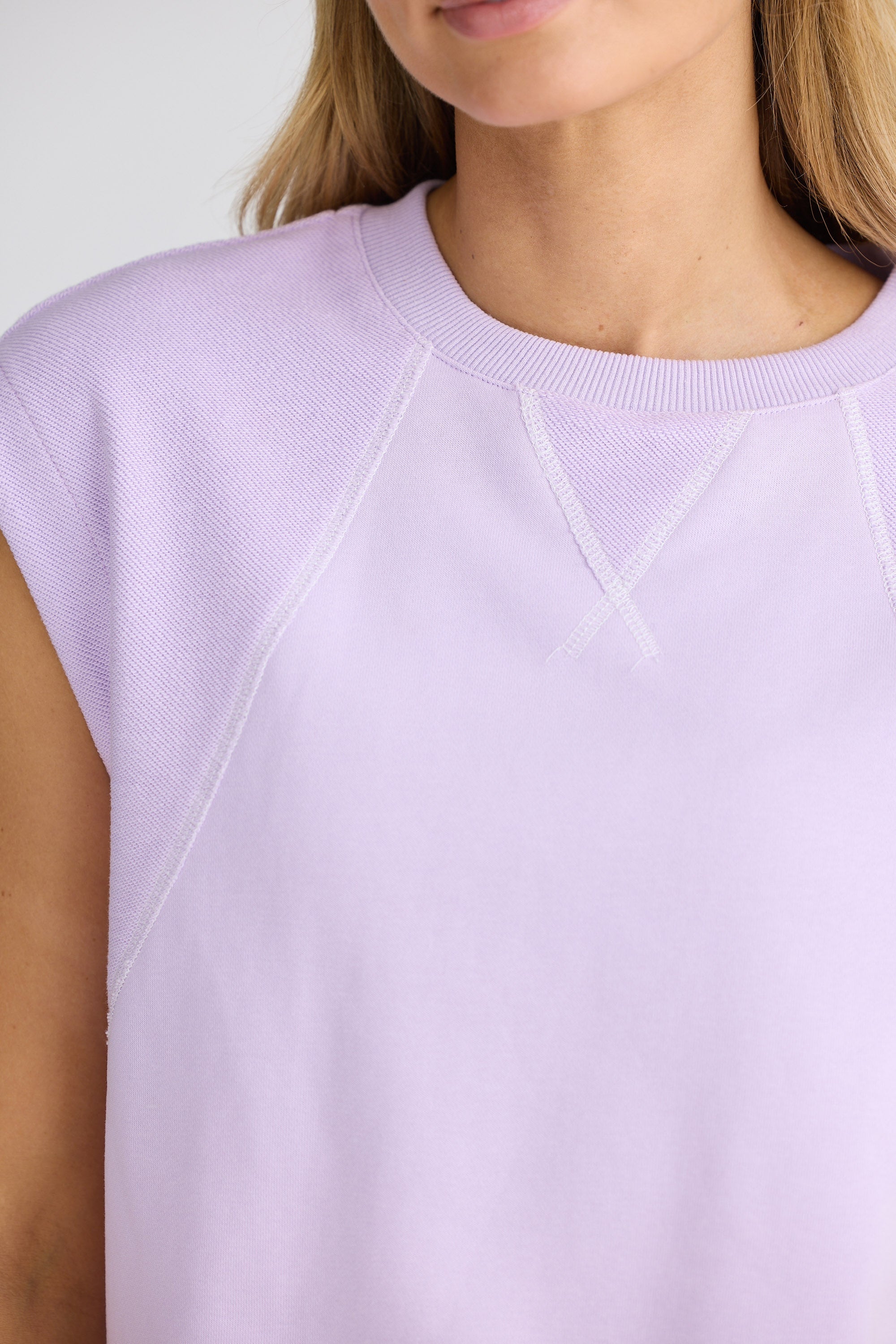 Close-up of a person wearing a light purple sleeveless top with a plain background