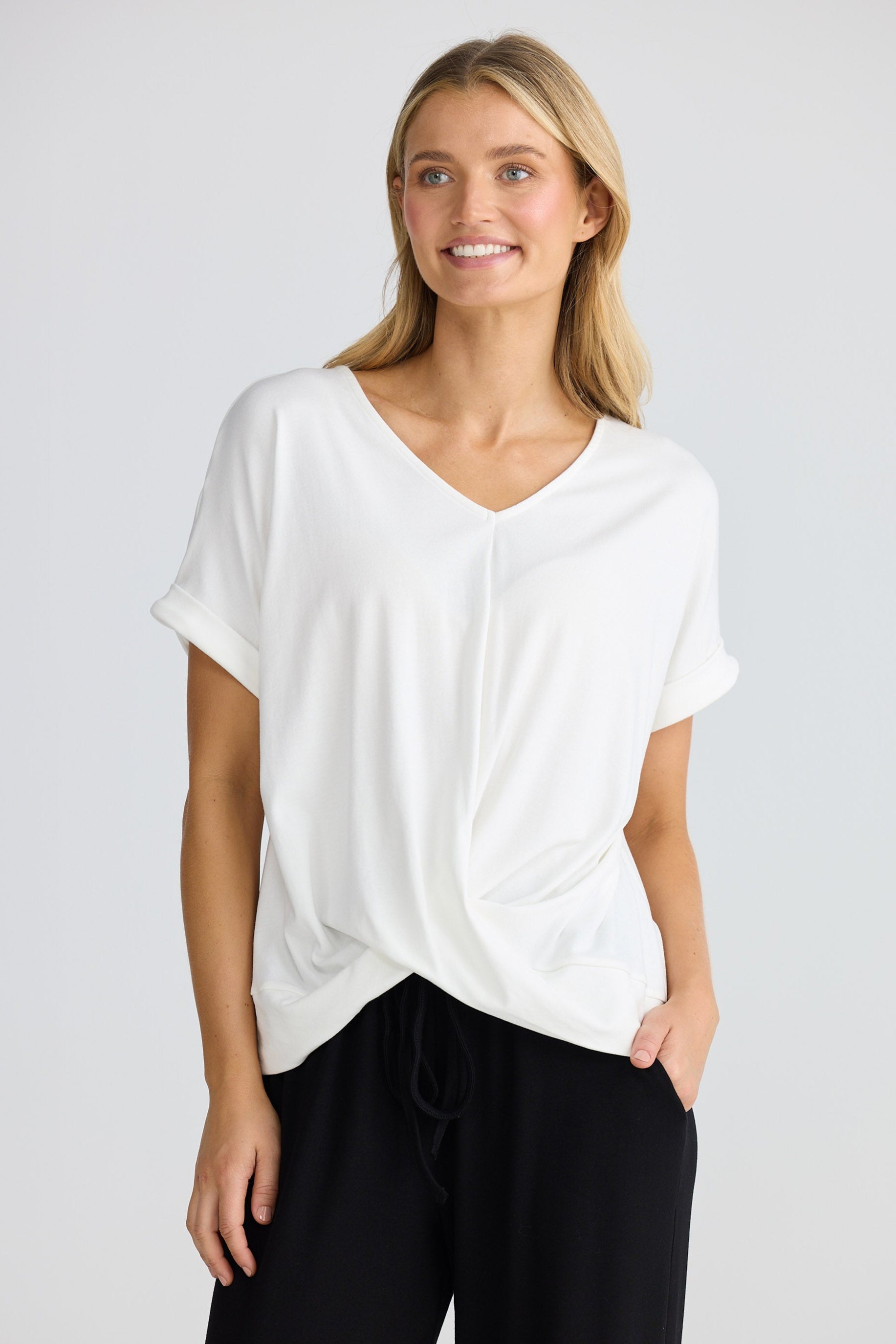 Woman wearing a white top and black pants on a plain background