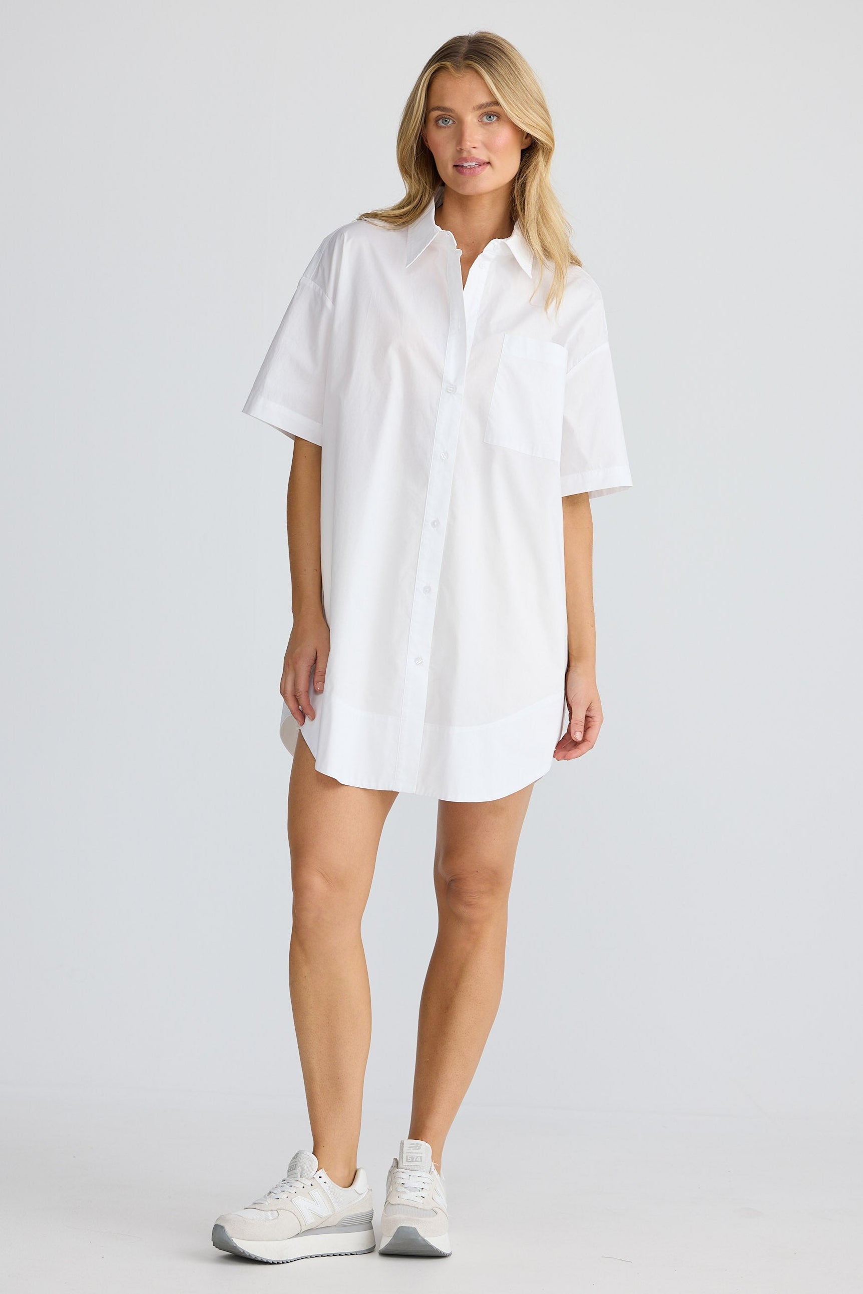 Woman wearing a white shirt dress on a plain background