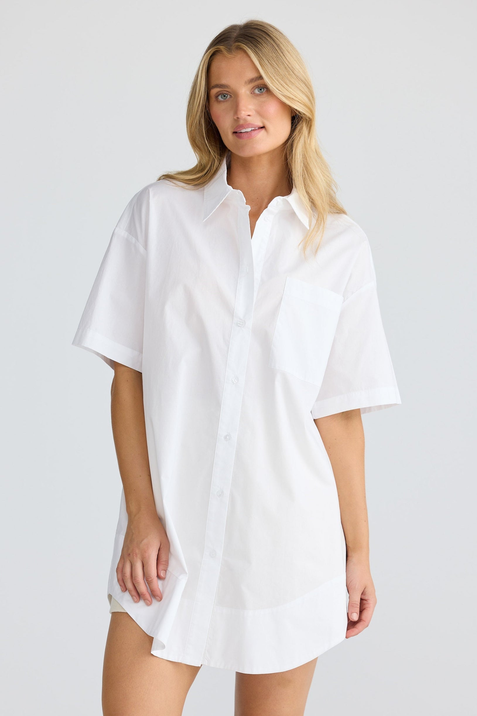 Woman wearing a white shirt dress against a plain background