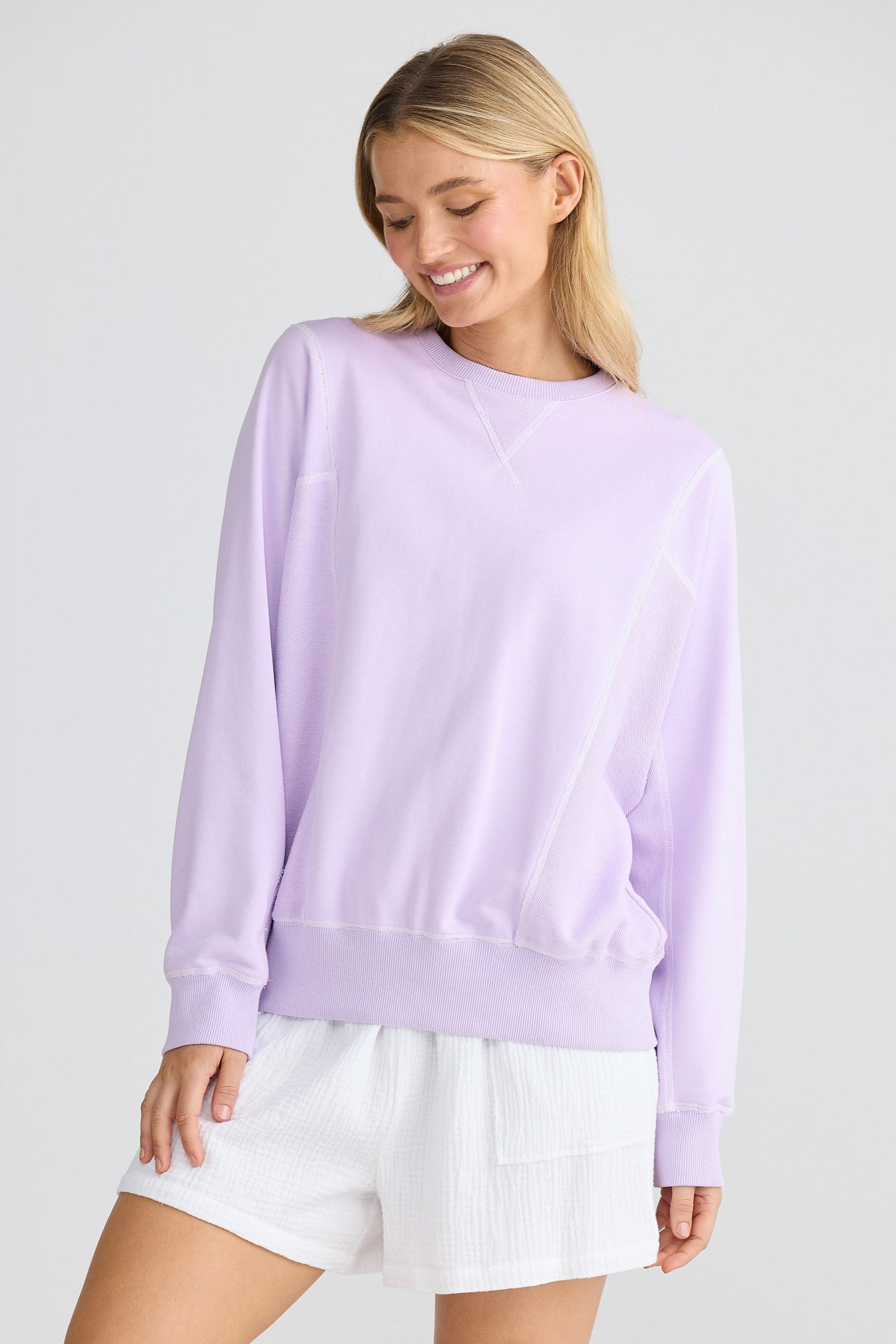 Woman wearing a light purple sweatshirt and white shorts on a plain background