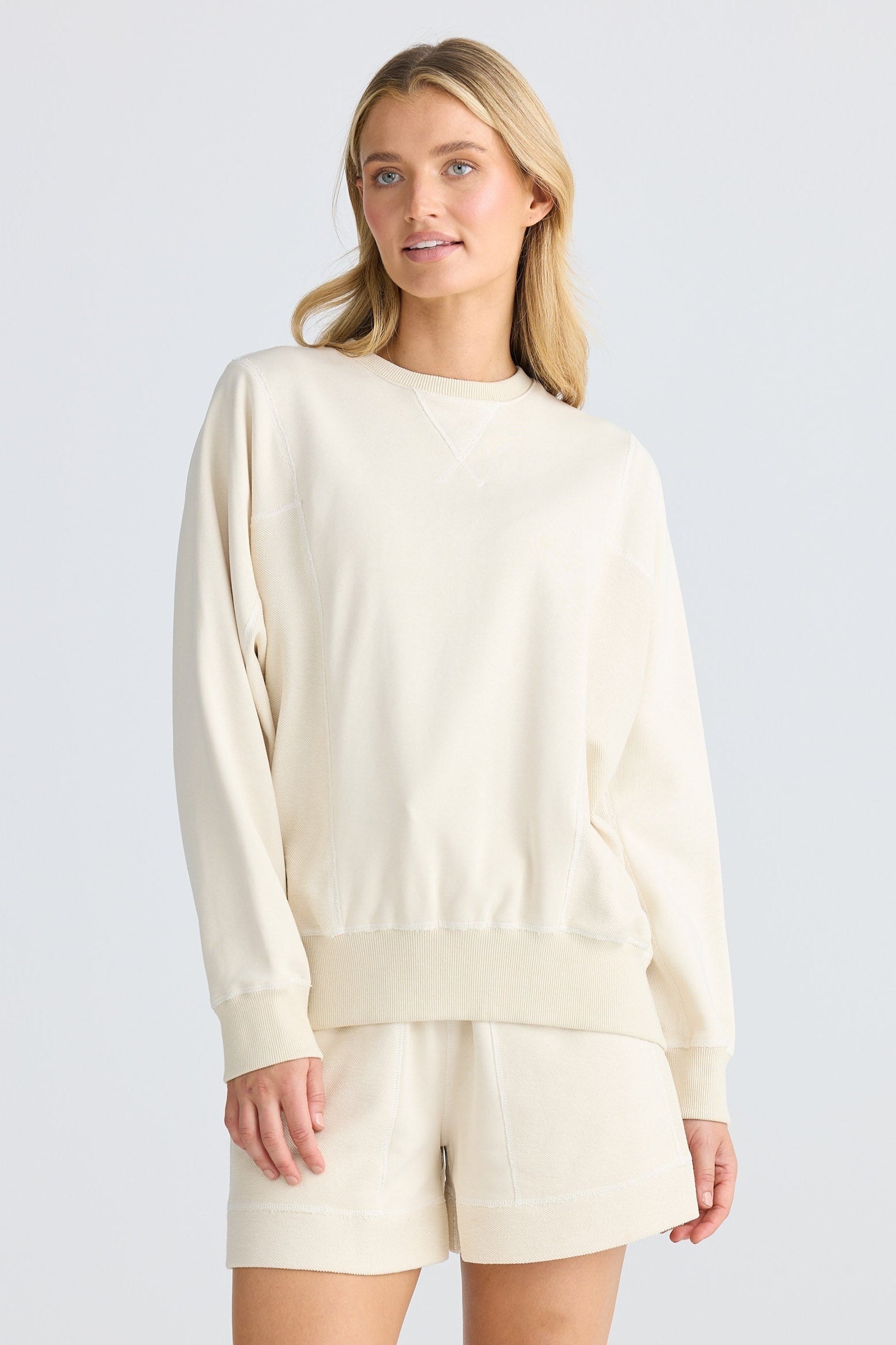 Woman wearing a cream-colored sweater and shorts on a white background