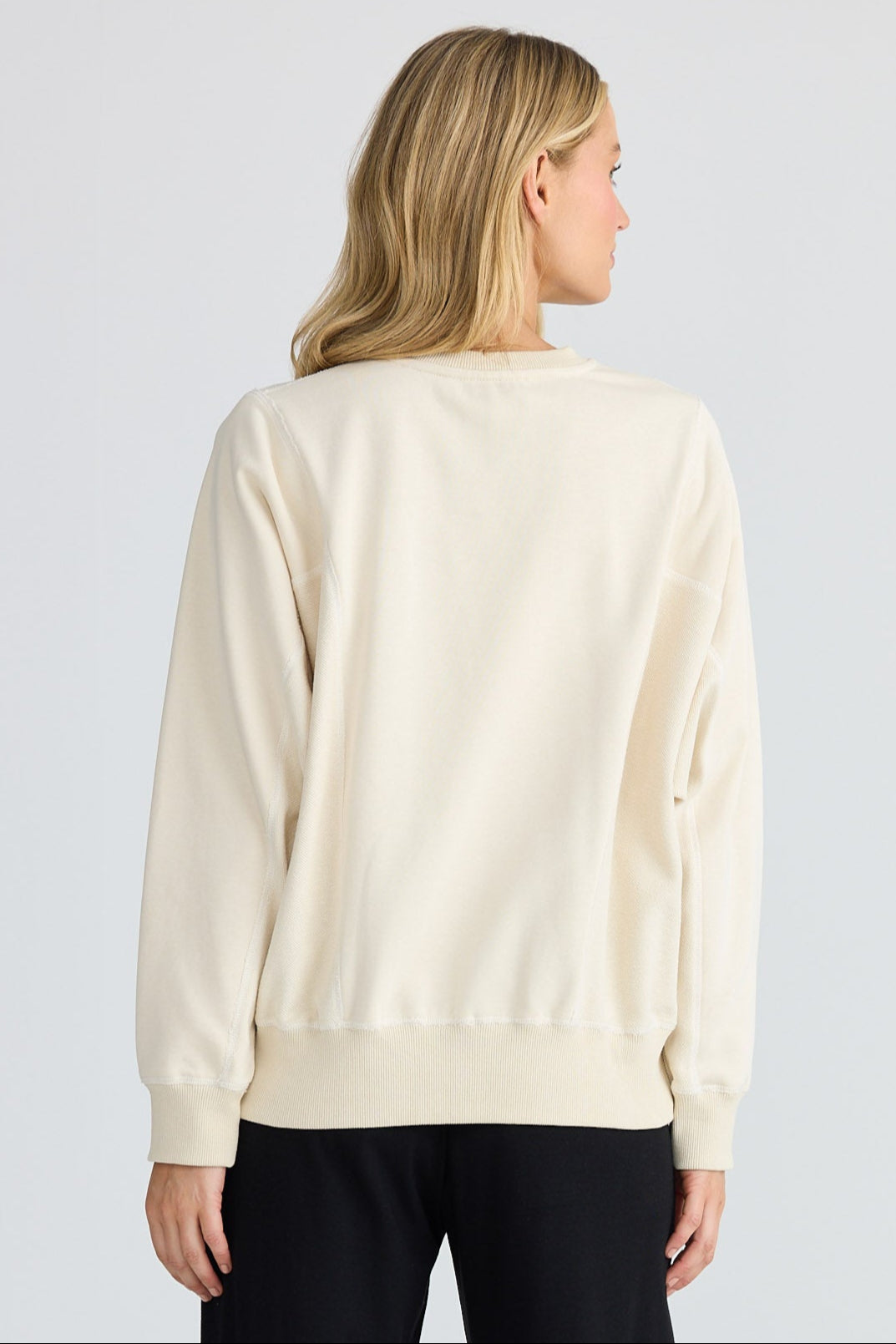 Woman wearing a cream sweater and black pants on a white background