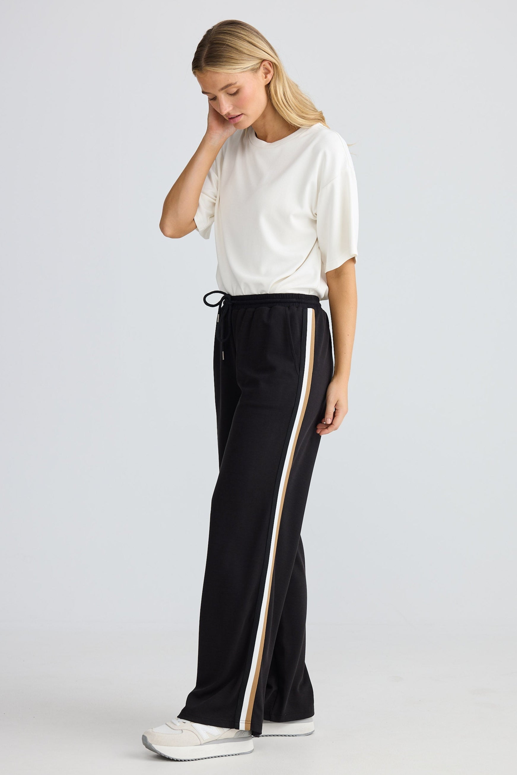 Woman wearing a white top and black pants with a side stripe on a white background