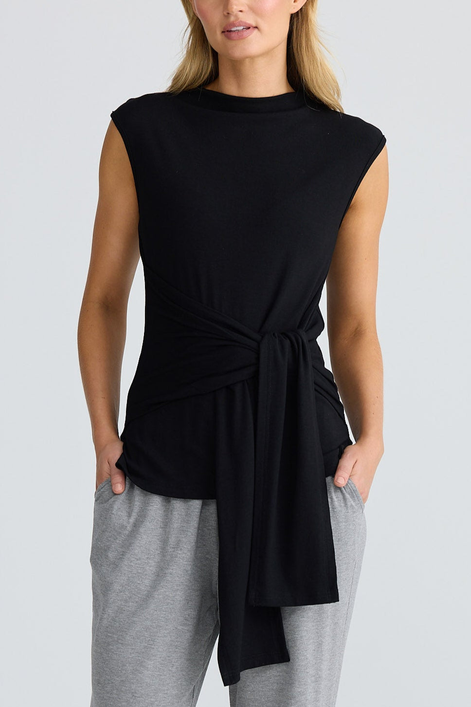 Woman wearing a black sleeveless top and gray pants on a white background