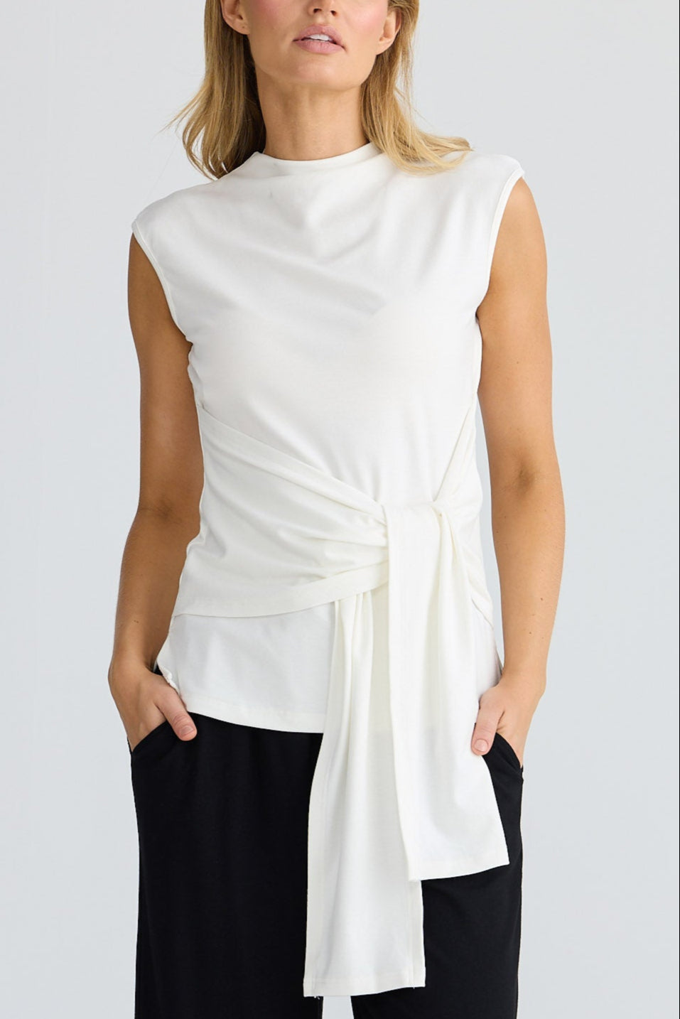 Woman wearing a white sleeveless top and black pants on a white background