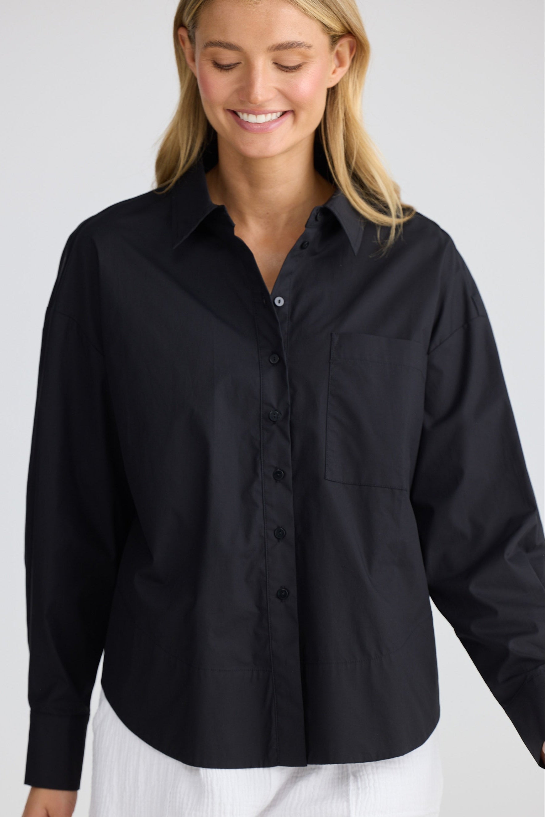 Woman wearing a black shirt and white pants on a plain background